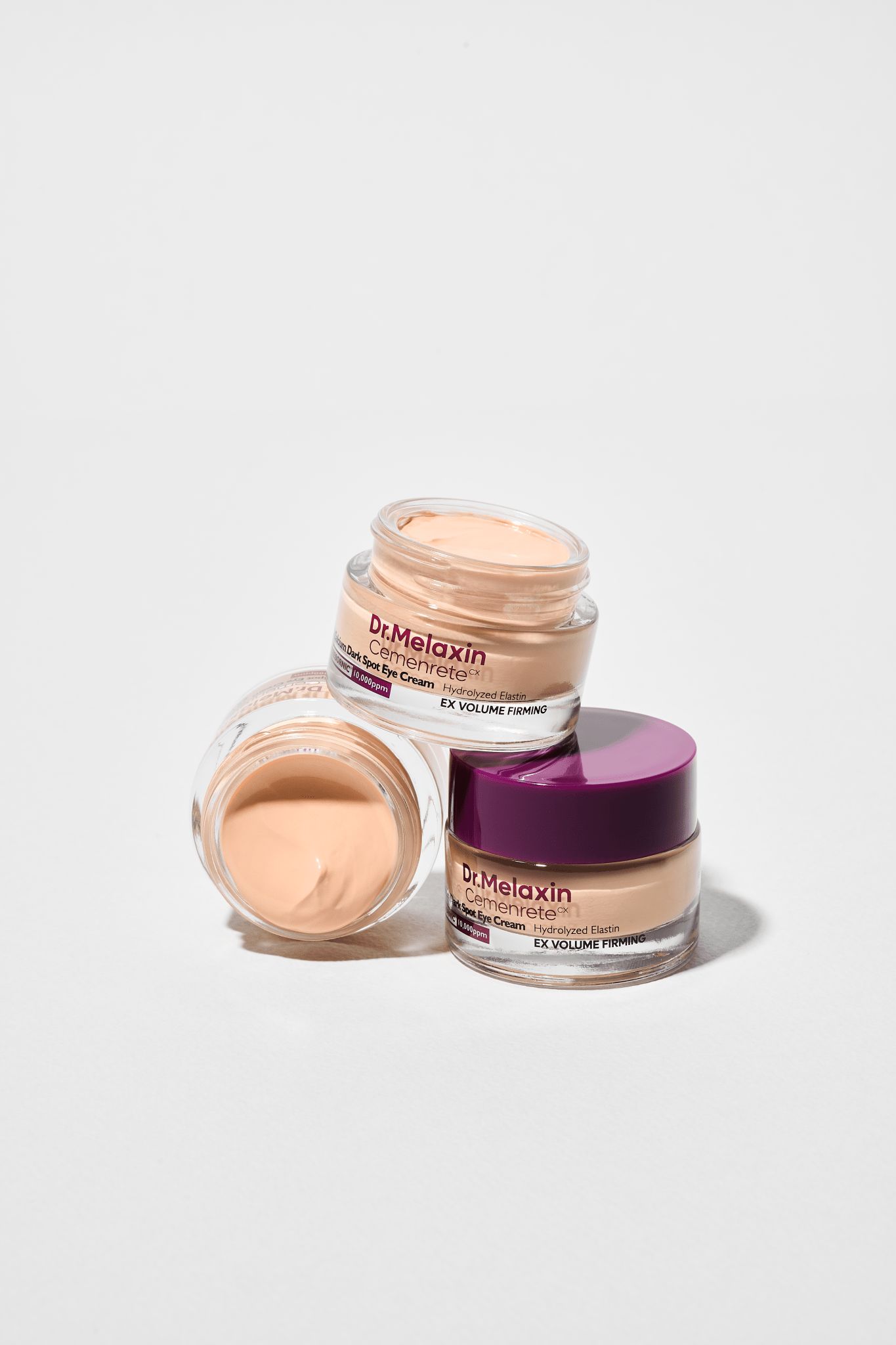 Drei Tiegel Dr.Melaxin Cemenrete Calcium Dark Spot Eye Cream. Lila Deckel, beige Creme. Weißer Hintergrund.
