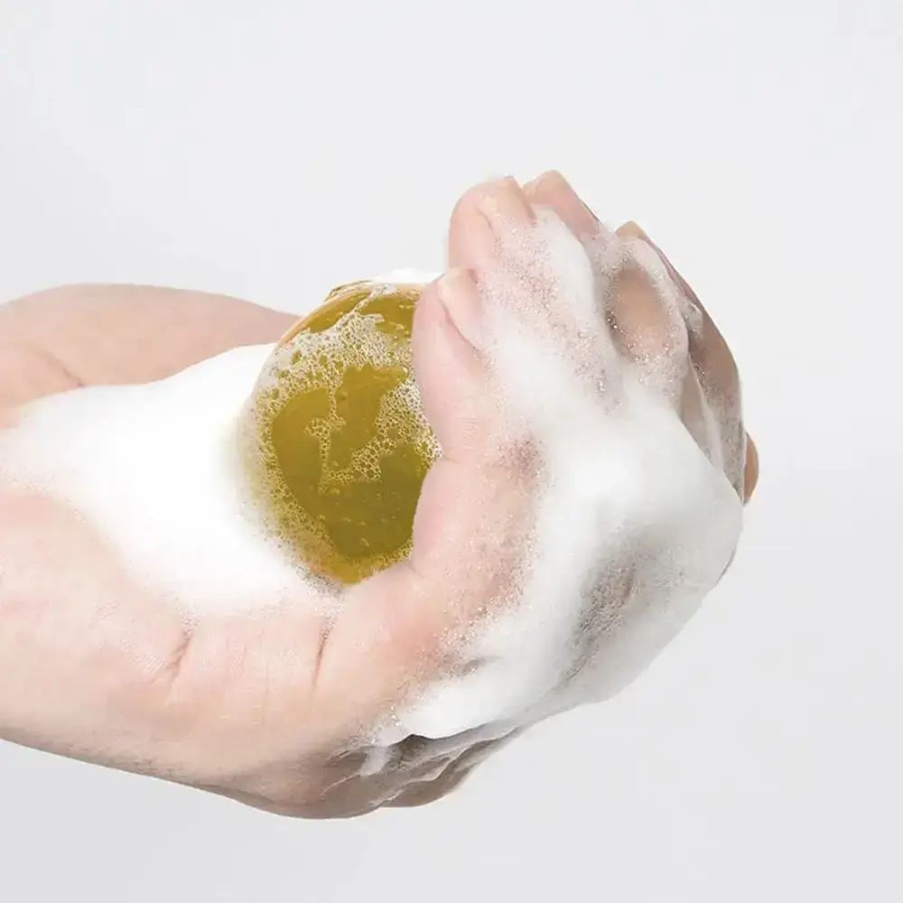 Hand, die eine gelbe Kugel mit Schaum hält. Nahaufnahme.