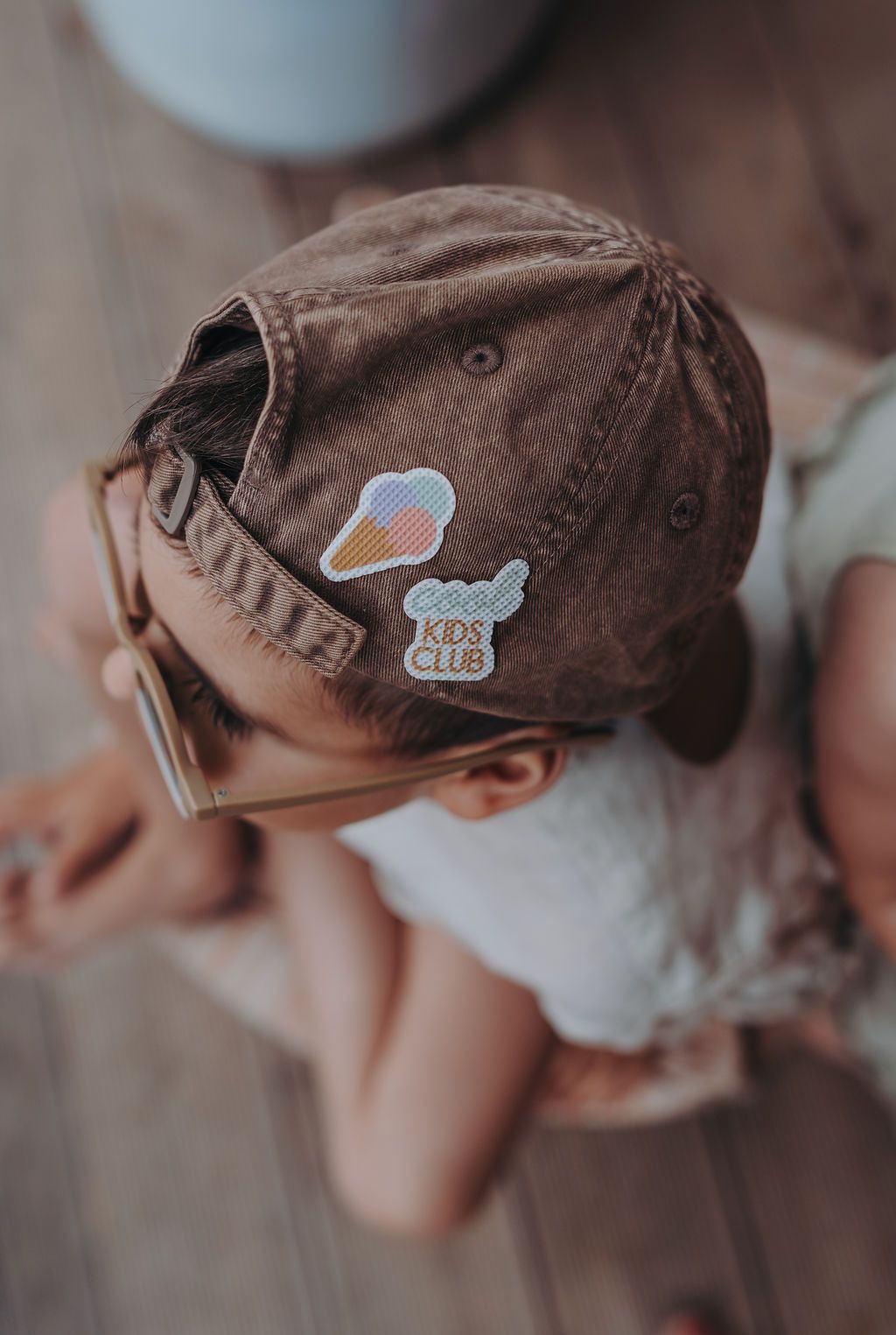 Kind mit brauner Kappe und Brille. Auf der Kappe sind zwei Sticker mit Eis und Wolken abgebildet.