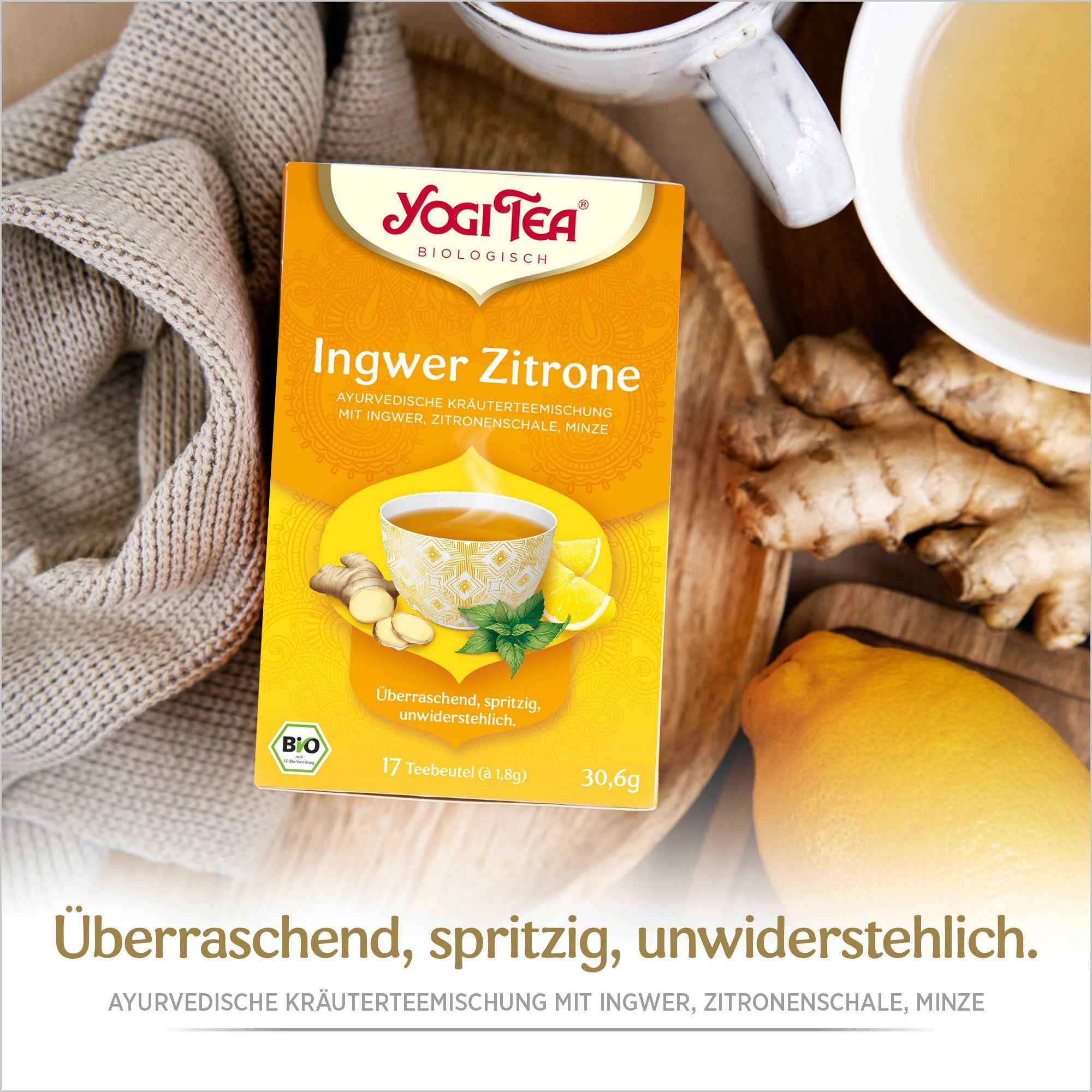 Yogi Tea Ingwer Zitrone Bio Gewürztee Packung auf Holztablett. Ingwer, Zitrone und Tasse Tee daneben. Text: Überraschend, spritzig, unwiderstehlich.