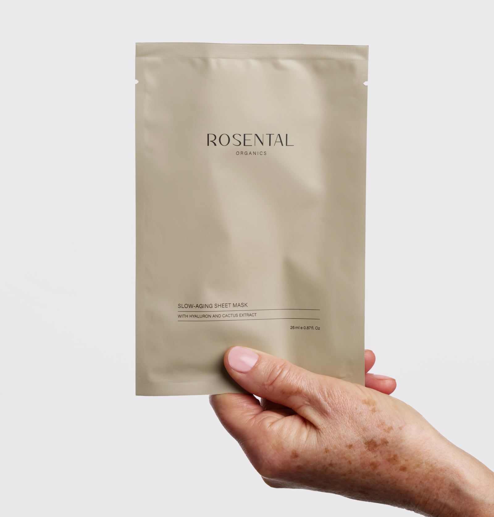 Beige Verpackung, Rosental Organics. Aufschrift: Slow-Aging Sheet Mask. Inschrift: Mit Hyaluron und Kaktus Extrakt. Gehalten von einer Hand.