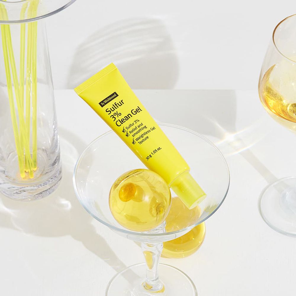 Gel-Tube, gelb, in einem Glas. Aufschrift Sulfur 3% Clean Gel. Umgeben von dekorativen Gläsern und Kugeln.