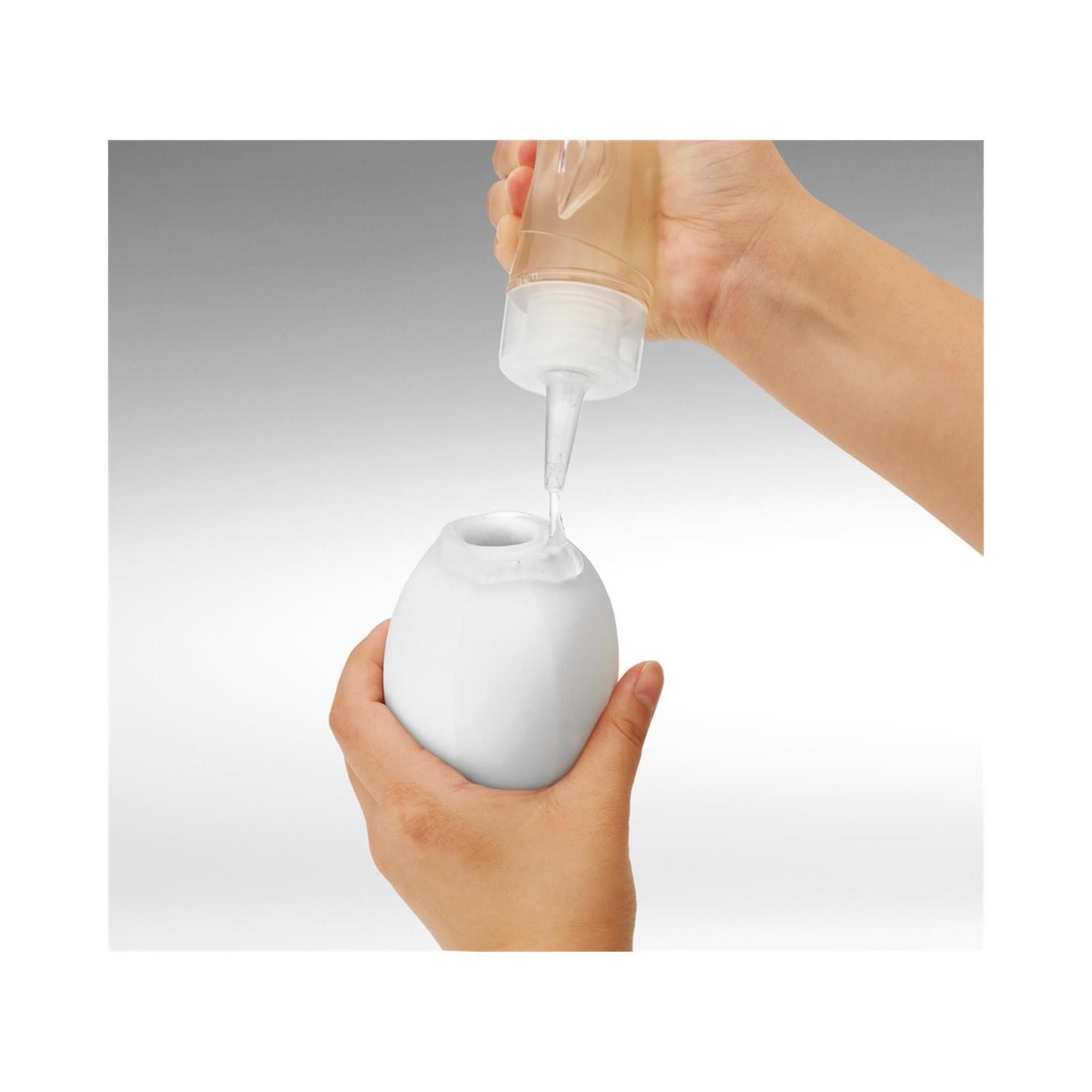 Hände füllen ein weißes, ovales Objekt mit Flüssigkeit aus einer Flasche.