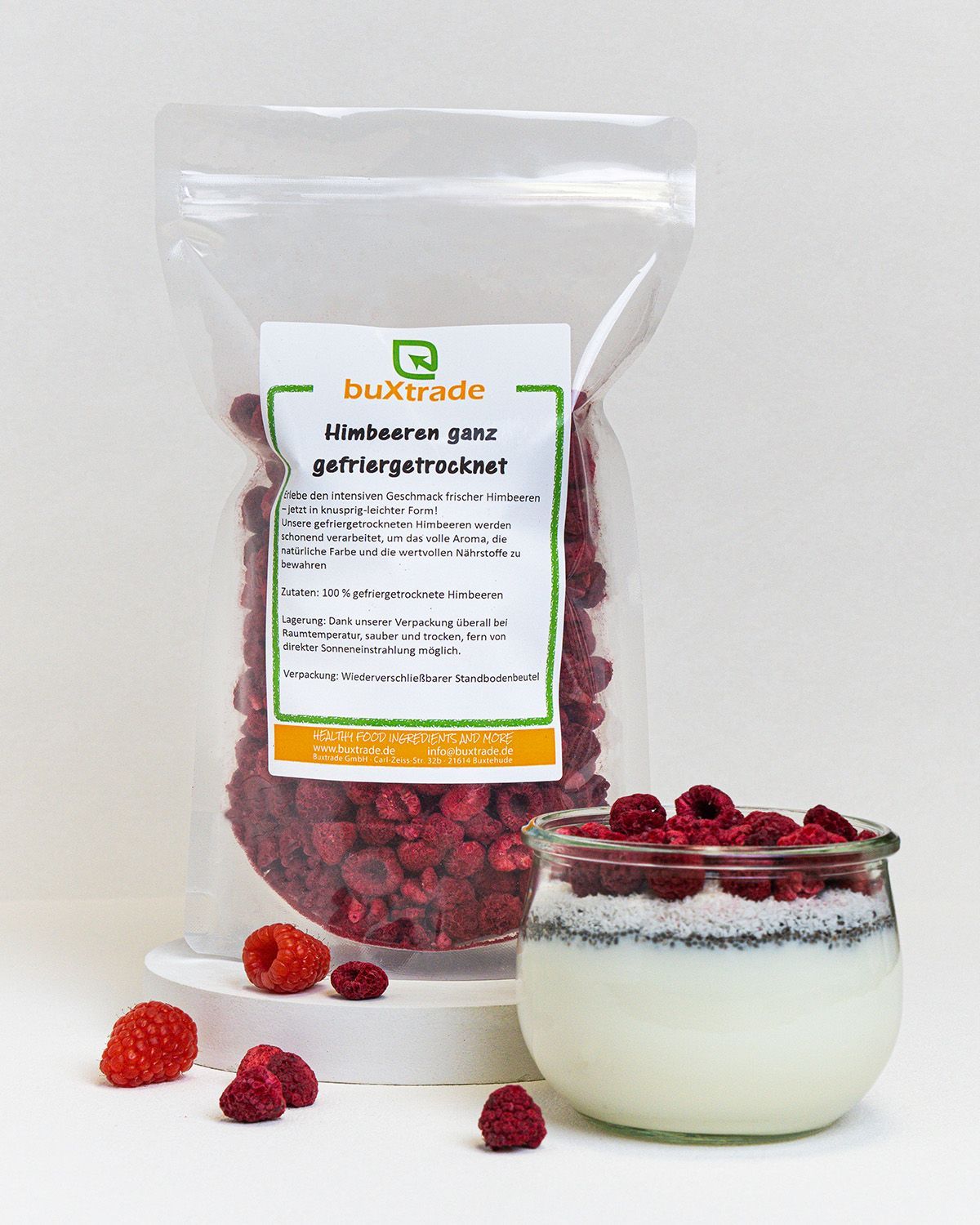 Verpackung mit gefriergetrockneten Himbeeren, daneben ein Glas mit Joghurt und Himbeeren. Einzelne Himbeeren liegen davor.