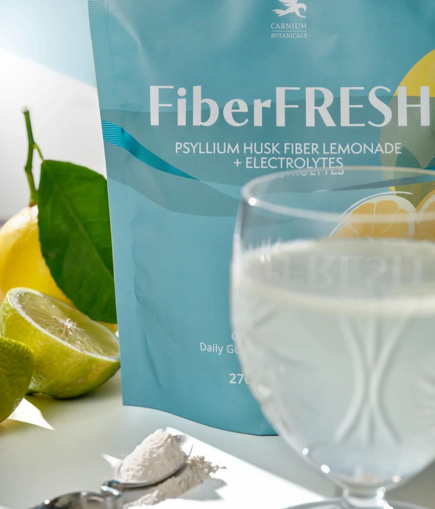 FiberFRESH-Beutel neben Glas mit Flüssigkeit, Löffel mit Pulver, Zitronen. Aufschrift: Psyllium Husk Fiber Lemonade + Electrolytes.