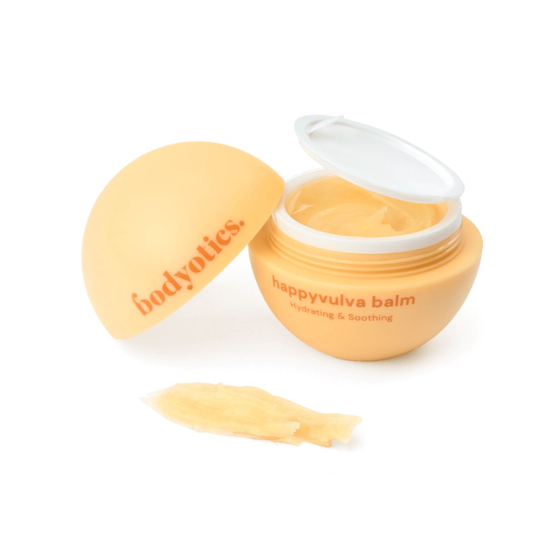 Beige Creme in einem runden Behälter mit Deckel. Aufschrift: happyvulva balm, bodyotics. Daneben ein Klecks Creme.