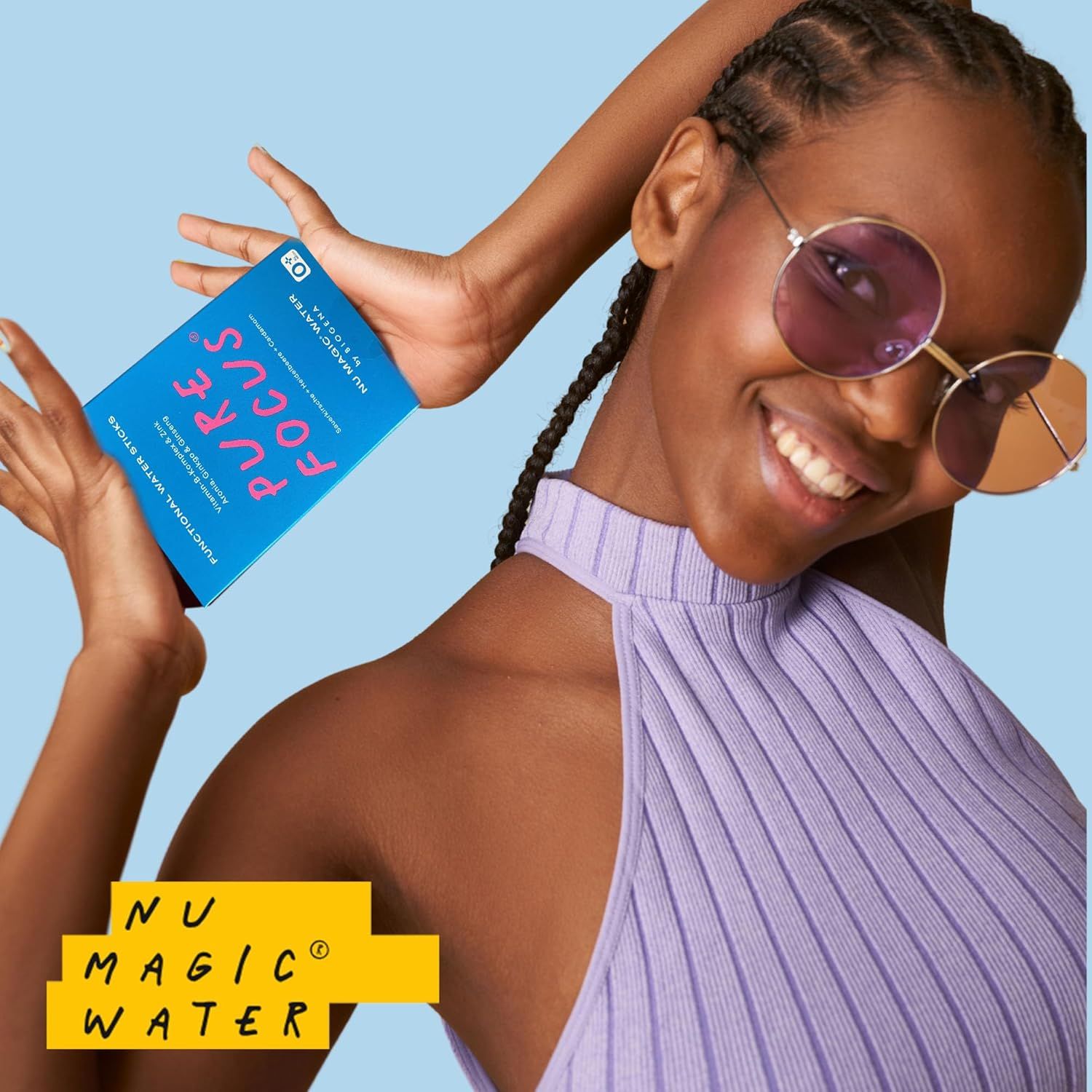 Frau hält blaue Schachtel "PURE FOCUS" und "NU MAGIC WATER" von BIOGENA. Sie trägt Brille und lila Oberteil. Hintergrund hellblau.
