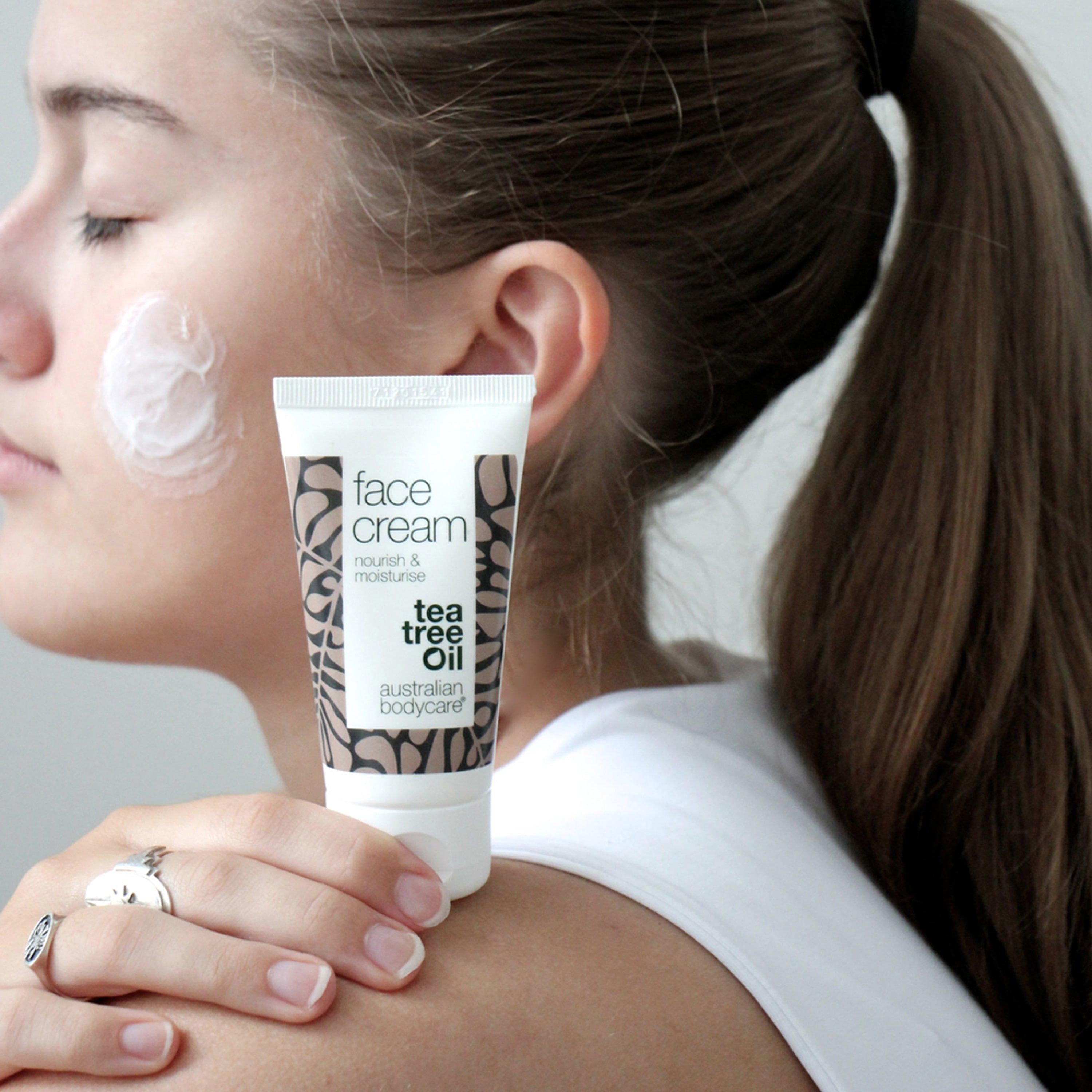 Frau mit Creme auf der Wange. Tube mit Text: face cream, tea tree oil. Marke: Australian Bodycare.
