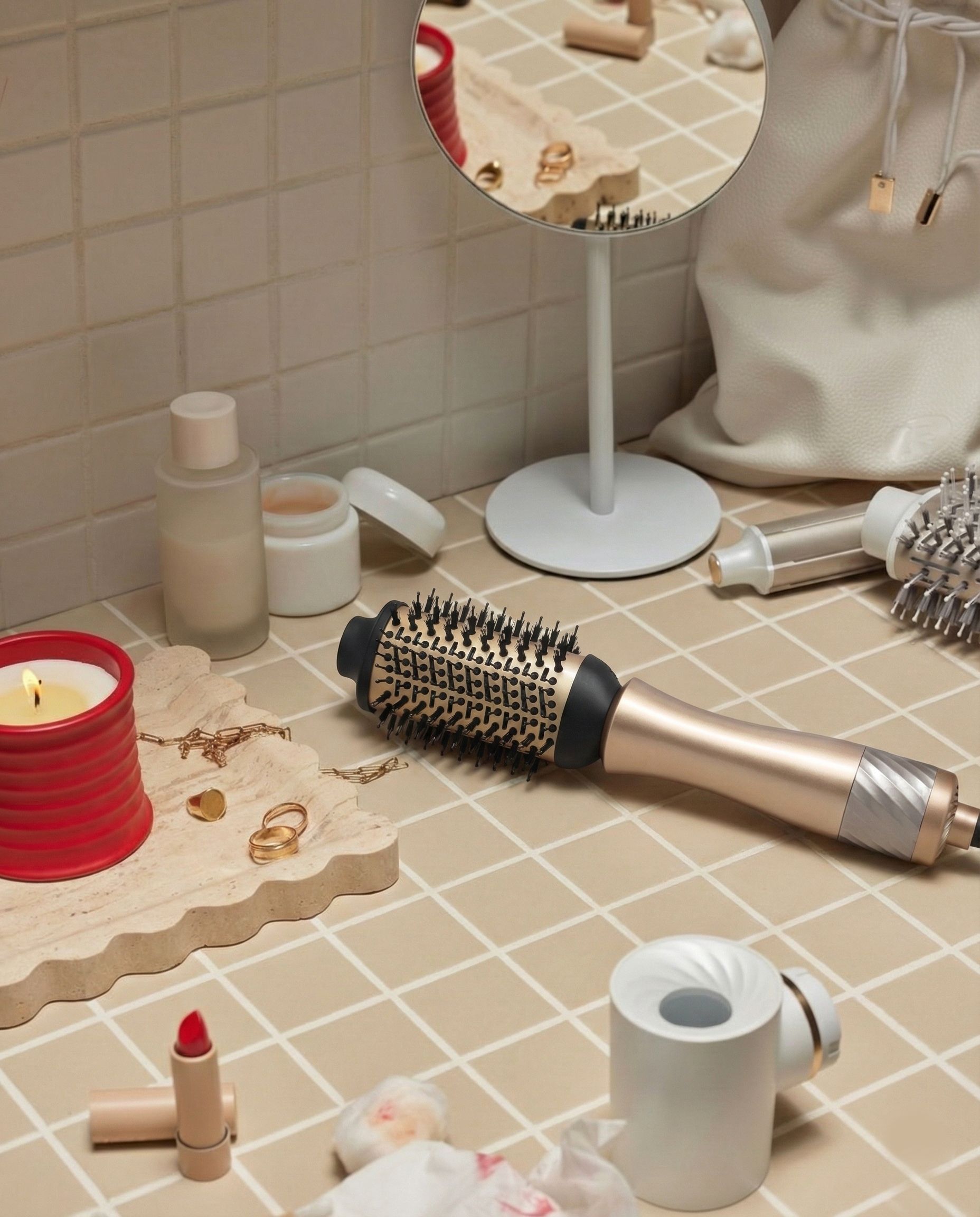 Goldene Stylingbürste liegt auf einer gefliesten Oberfläche neben Kosmetik und Kerzen.