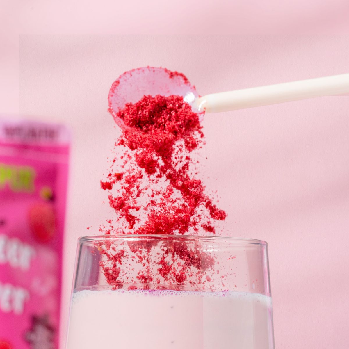 Löffel mit Himbeerpulver über einem Glas mit rosa Flüssigkeit. Hintergrund: rosa.