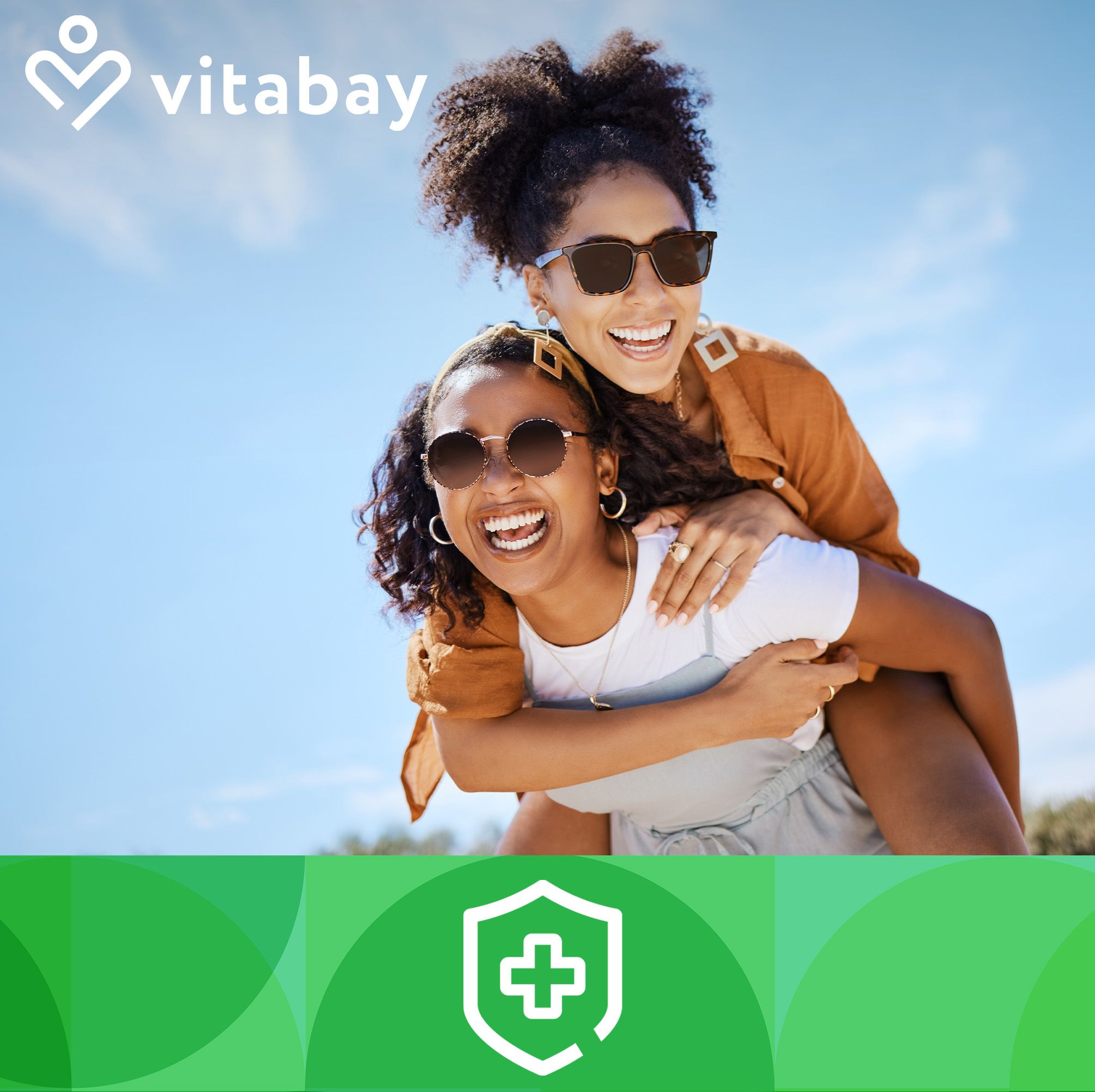 Zwei Frauen lachen im Freien. Eine trägt die andere auf dem Rücken. Beide tragen Sonnenbrillen. Im Hintergrund blauer Himmel.