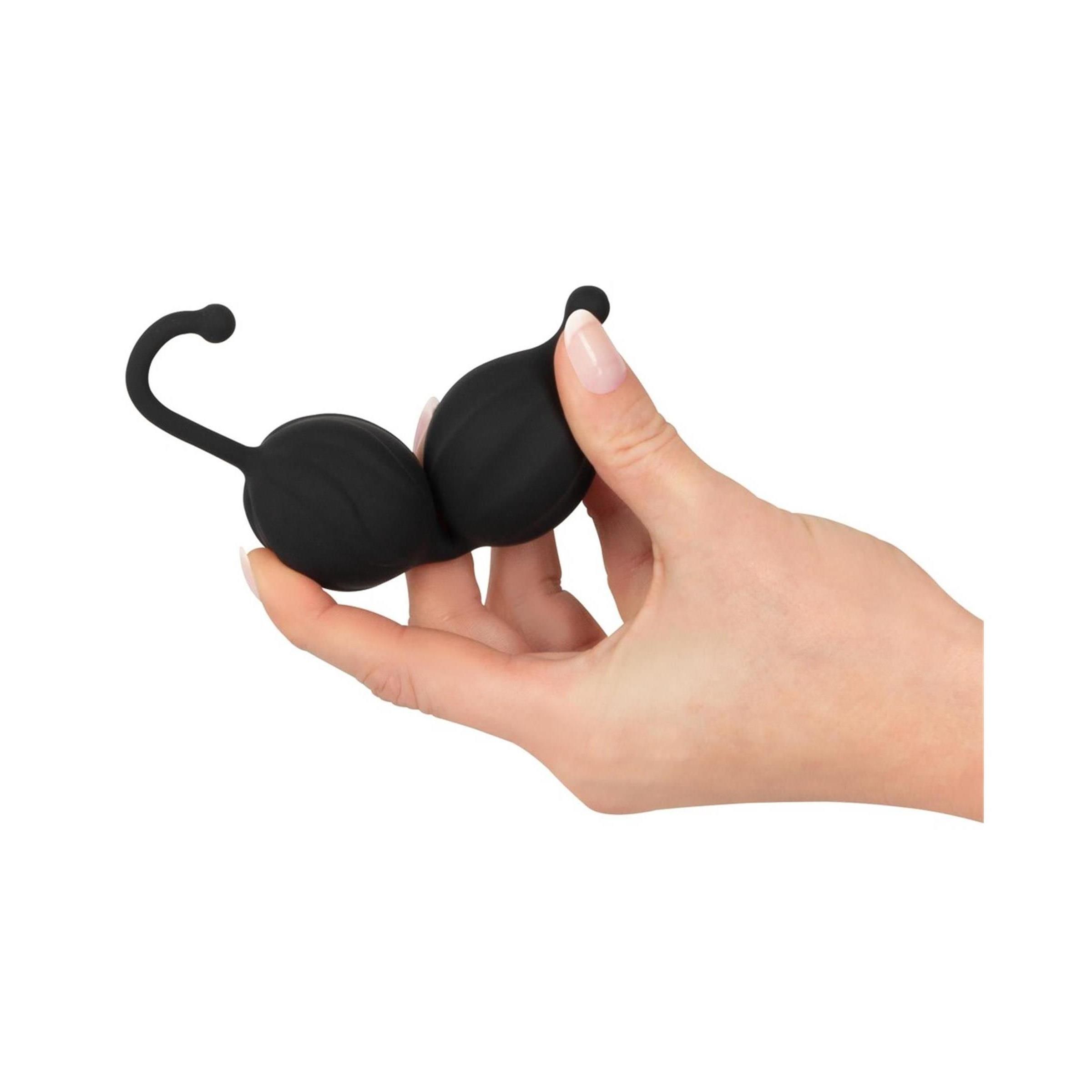 Zwei schwarze, ovale Silikonkugeln in einer Hand gehalten. Mit Verlängerung und kleiner Kugel am Ende.