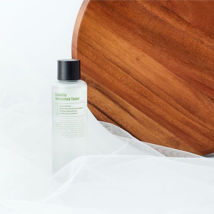 Tonerflasche mit schwarzem Deckel auf Holzbrett und weißem Stoff. Aufschrift: Centella Unscented Toner.