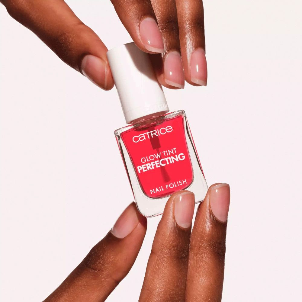 Hände halten Nagellackflasche. Roter Nagellack, weißer Deckel. Aufschrift: Catrice, Glow Tint Perfecting, Nail Polish.
