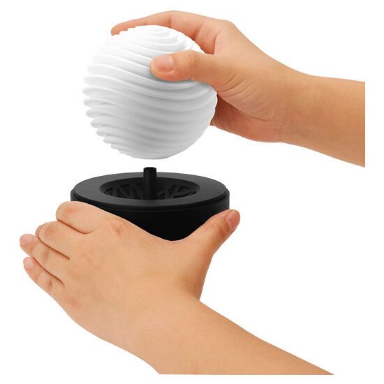 Hände halten ein weißes, kugelförmiges Produkt und einen schwarzen Sockel. Das Produkt wird vom Sockel getrennt.