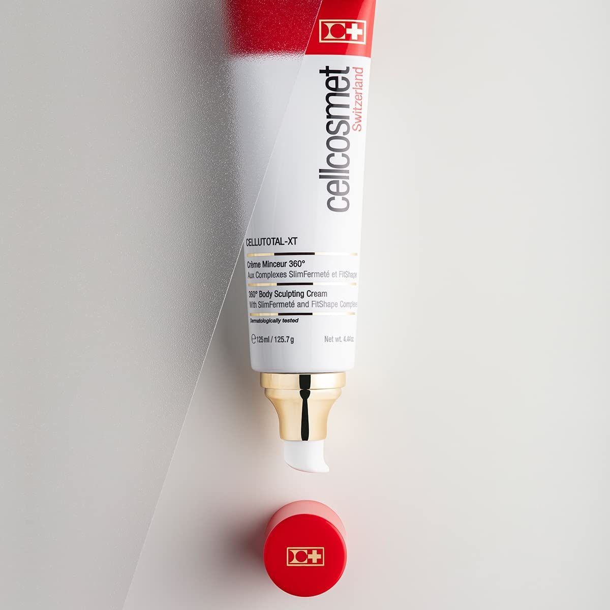 Geöffnete Tube mit rotem Deckel. Produktname: Cellcosmet CelluTotal XT. Goldfarbener Pumpkopf. Creme wird herausgedrückt.