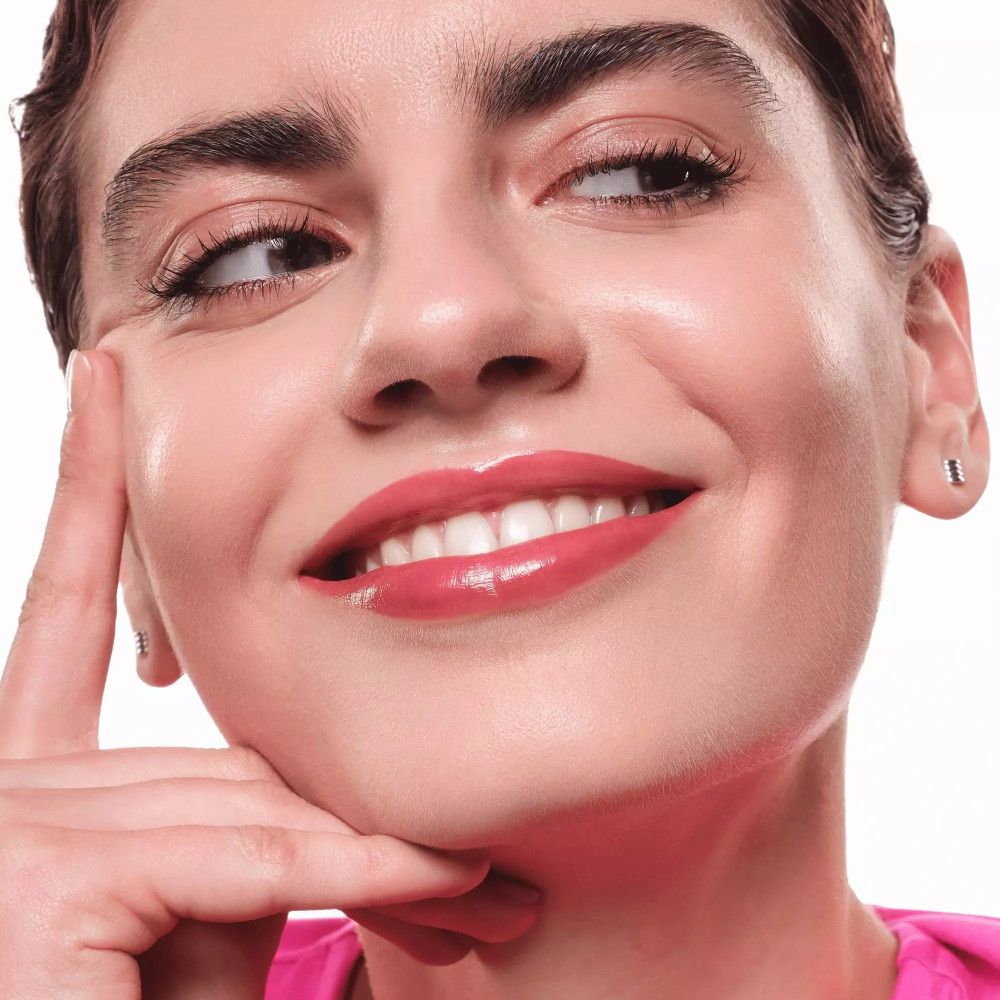 Porträt einer Frau mit rosa Lippen. Sie lächelt und berührt ihr Gesicht. Ohrringe.