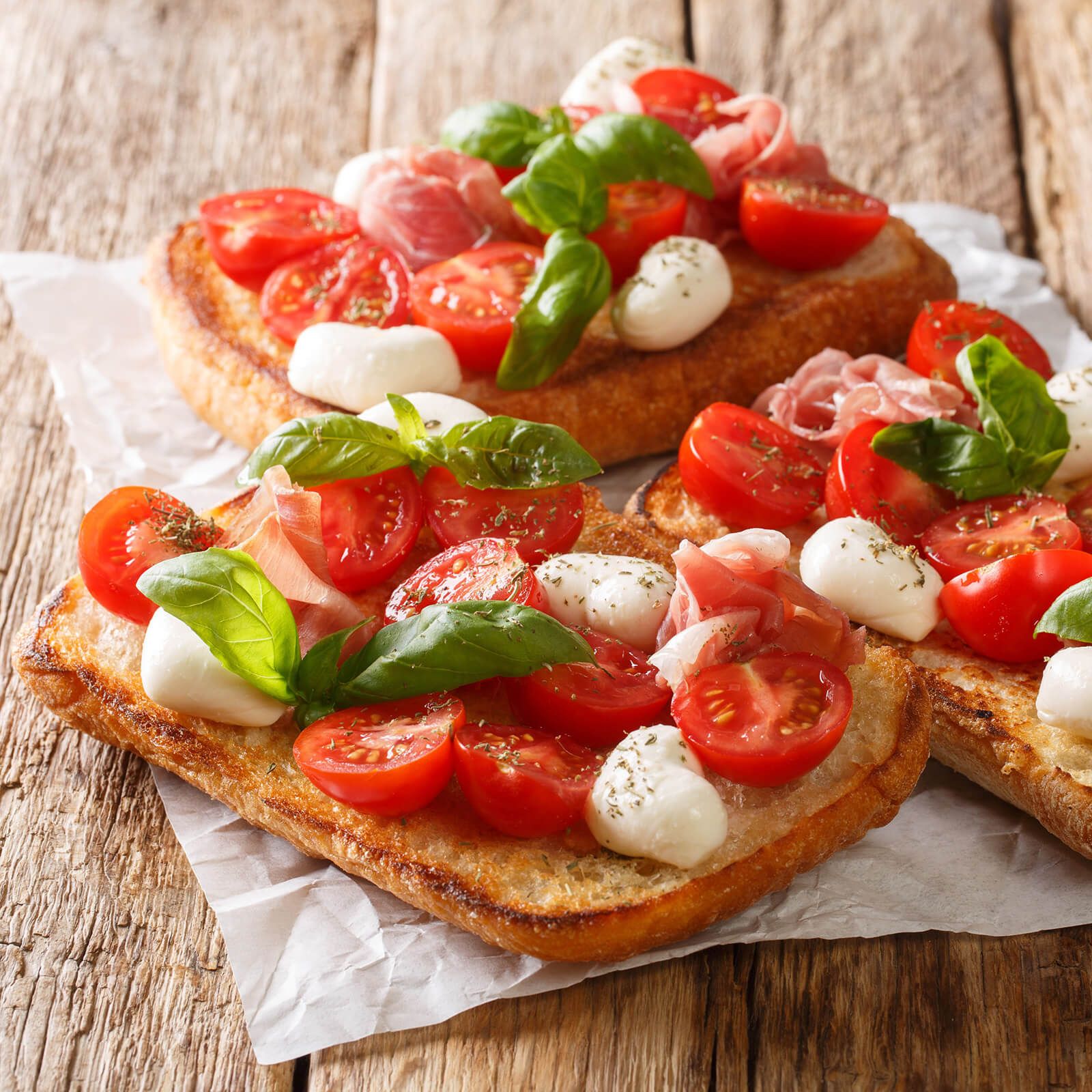 Ciabattini-Scheiben mit Tomaten, Mozzarella, Schinken und Basilikum.