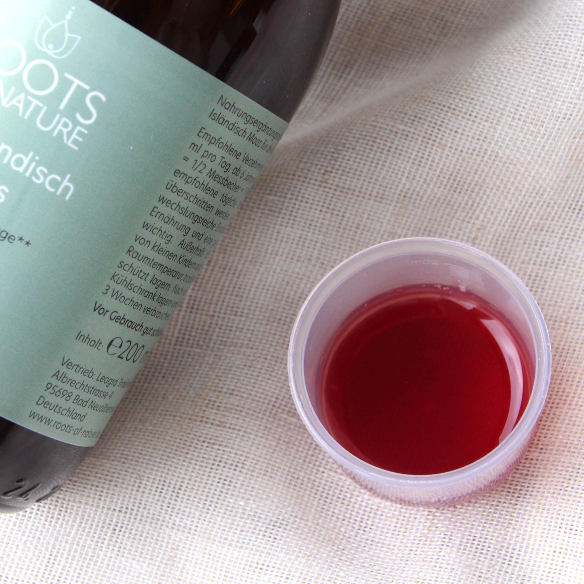 Braune Glasflasche mit Etikett. Daneben ein Messbecher mit roter Flüssigkeit. Text: ROOTS OF NATURE, Isländisch Moos.