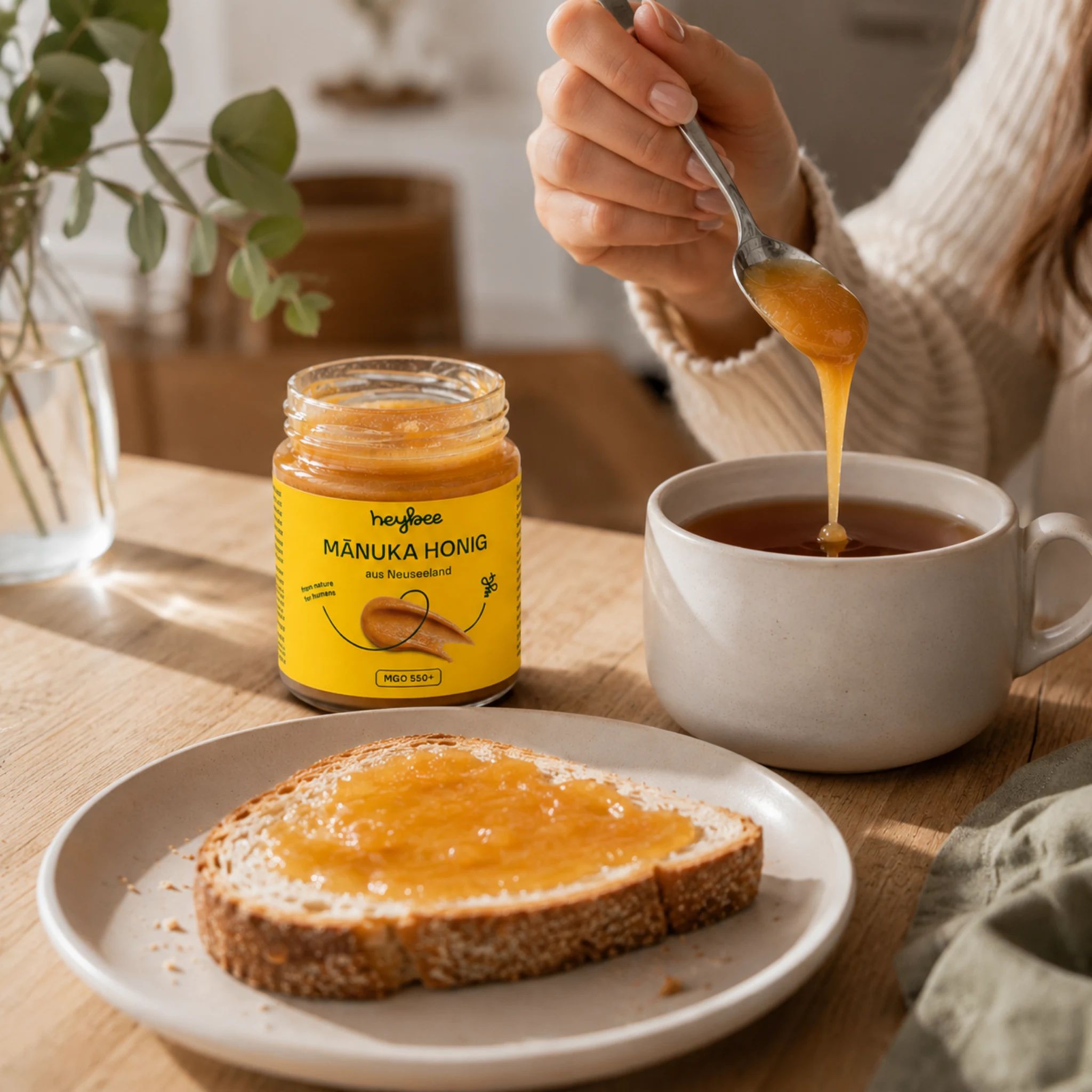 Glas Manuka Honig MGO 550+ auf Toast. Löffel mit Honig über einer Tasse Tee.