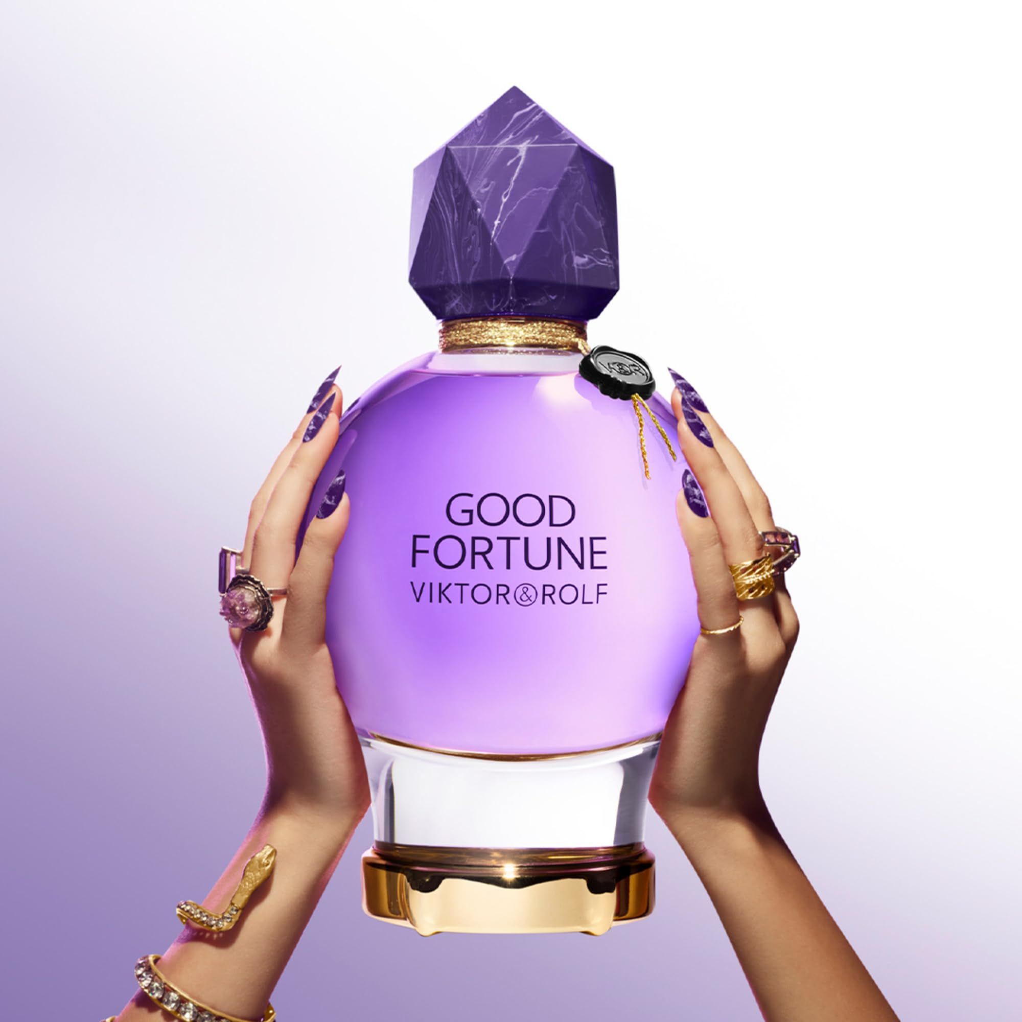 Violetter Flakon mit Kristallverschluss, gehalten von Händen mit Nägeln und Ringen. Aufschrift: Good Fortune, Viktor & Rolf.