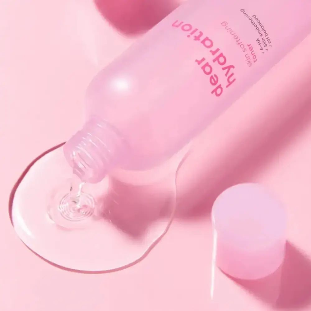 Eine rosa Flasche mit der Aufschrift 'dear hydration' kippt und gibt eine klare Flüssigkeit ab. Der Deckel liegt daneben.