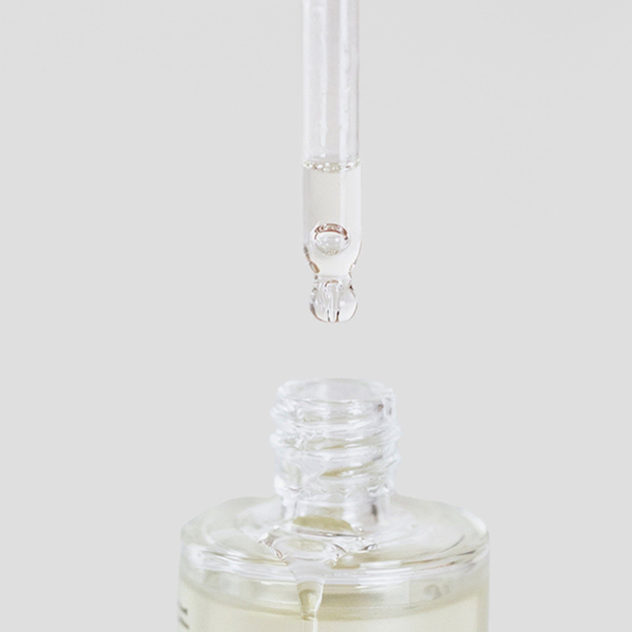 Nahaufnahme einer Glasflasche mit Pipette. Tropfen Öl am Ende der Pipette.