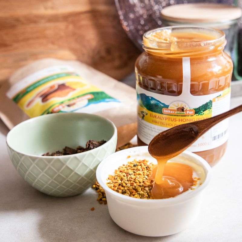 Honig wird mit einem Löffel aus einem Glas in eine Schale gegossen. Etikett sichtbar.