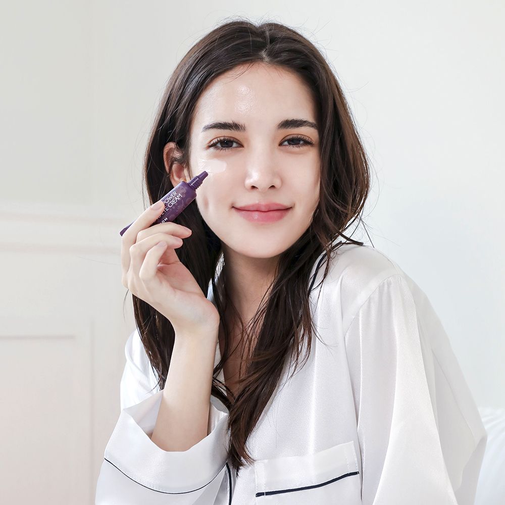 Frau hält Tube MIZON Collagen Power Firming Eye Cream. Lila Tube, rosa Kappe. Text: Collagen Power Firming Eye Cream.