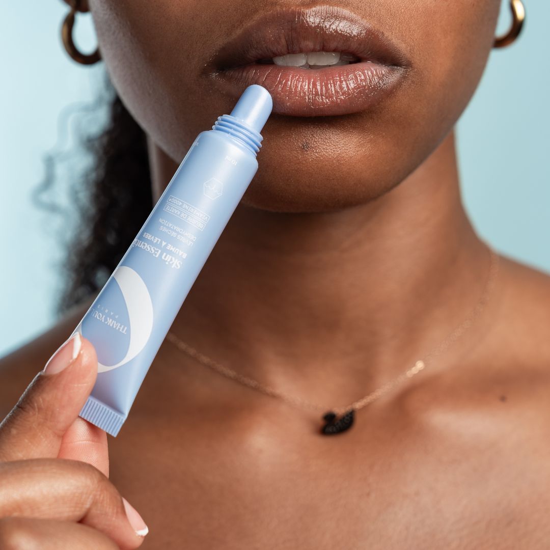 Person trägt hellblaue Tubenlippenpflege auf. Nahaufnahme der Lippen. Produktname und Schriftzug sichtbar.