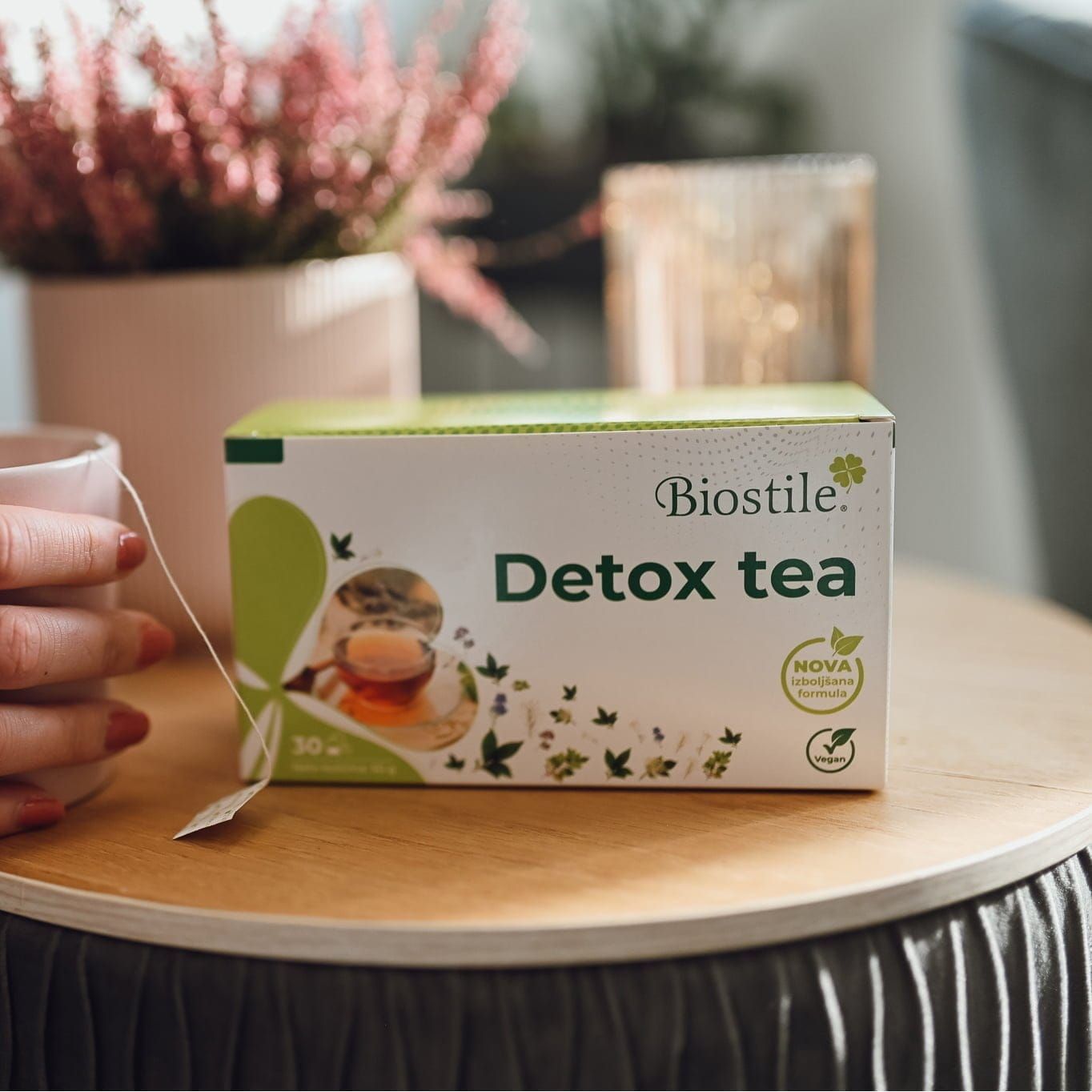 Eine Person hält eine Tasse Tee mit einem Teebeutel. Daneben eine Packung Biostile Detox Tea.
