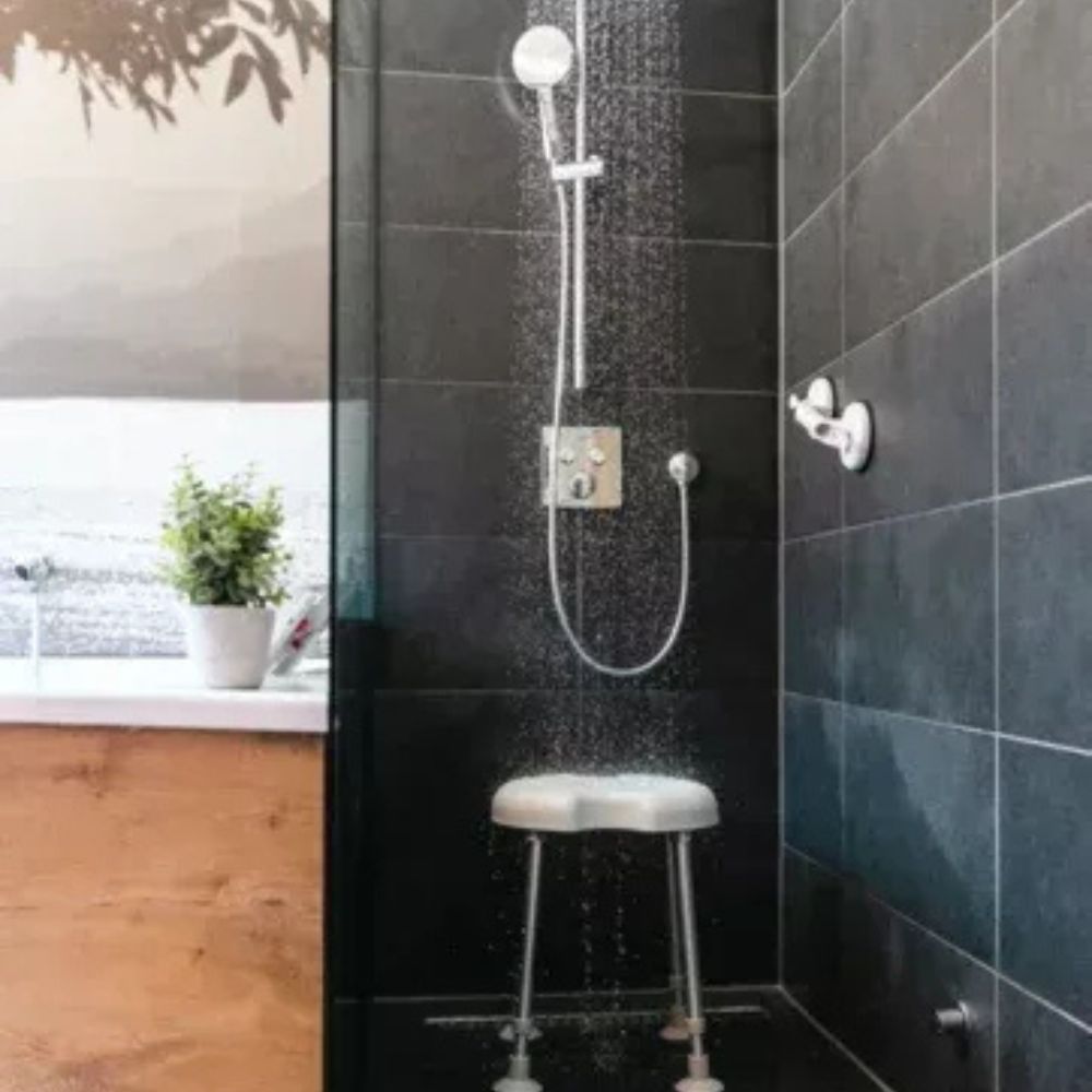 Duschszene mit Duschhocker. Der Hocker steht unter einer Dusche mit fließendem Wasser. Schwarze Fliesen.