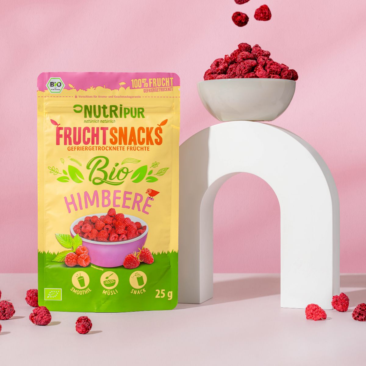 Beutel mit gefriergetrockneten Bio-Himbeeren, Schale mit Himbeeren, weißer Bogen, Himbeeren verstreut.