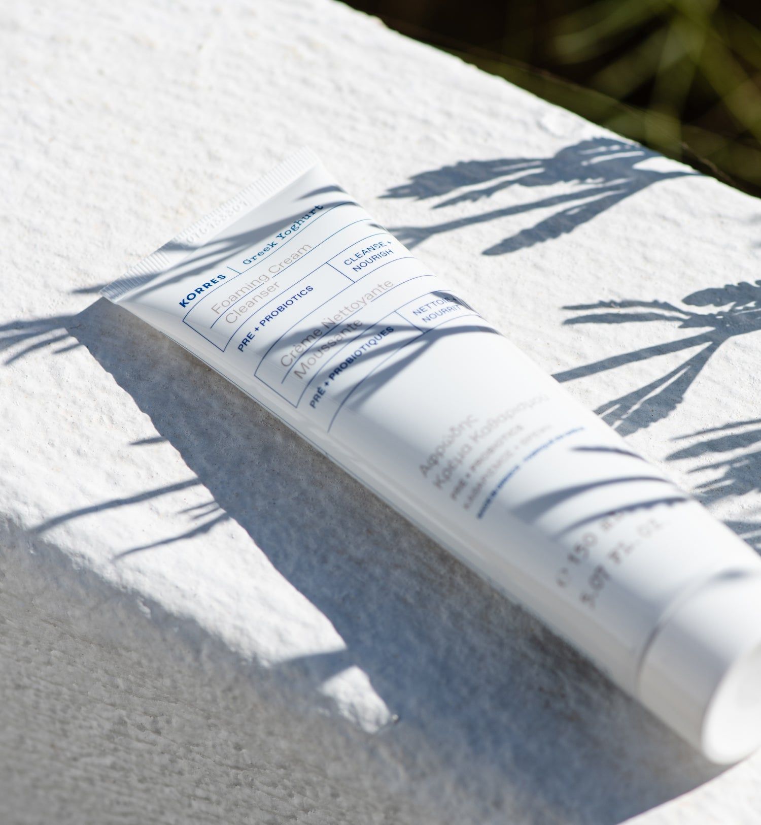 Weiße Tube mit Produktbeschriftung. Liegt auf weißem Handtuch, Schatten.