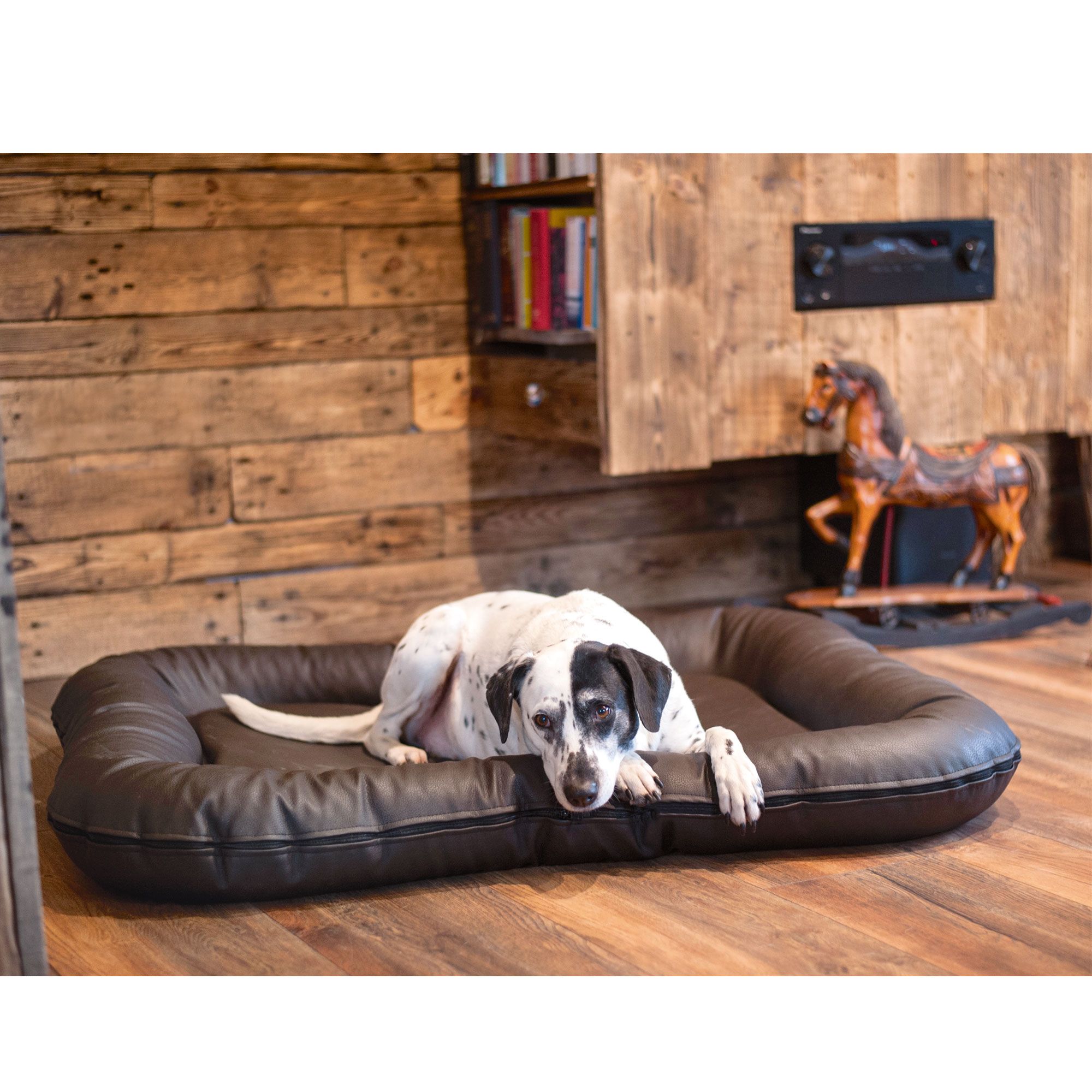 Braunes Hundebett aus Kunstleder. Ein Hund liegt auf dem Bett in einem Raum.