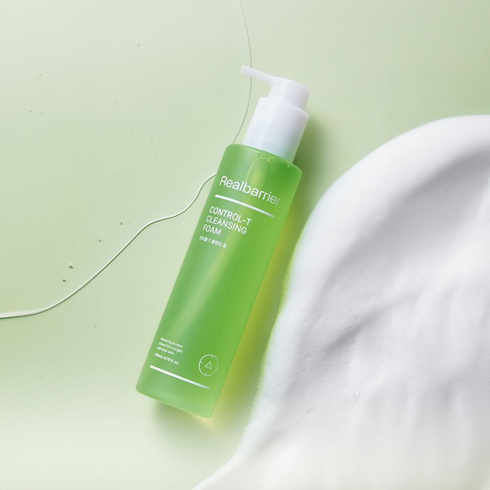 Grüne Flasche mit weißem Pumpverschluss, umgeben von Schaum. Aufschrift: Realbarrier, CONTROL-T CLEANSING FOAM.