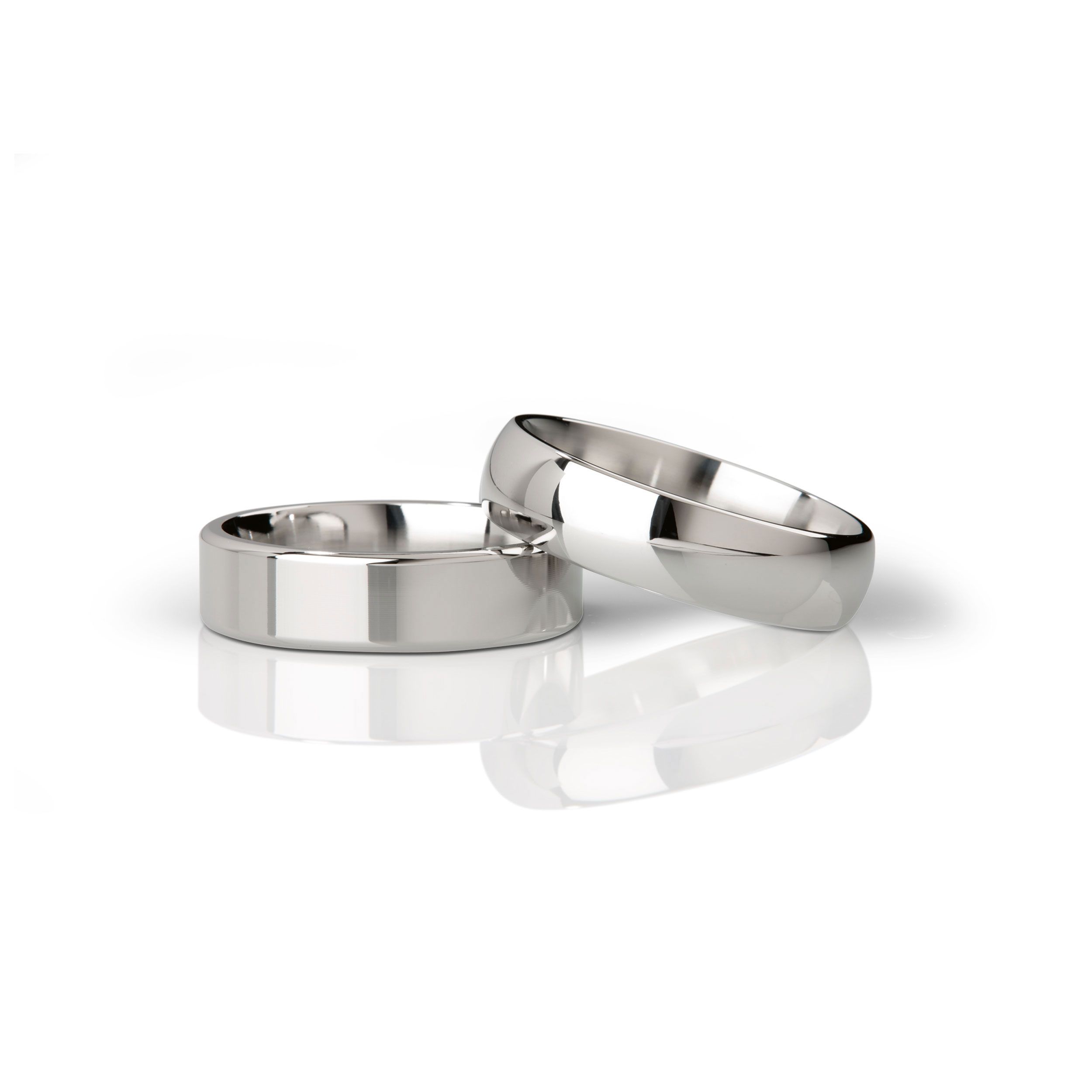 Zwei Ringe aus poliertem Metall. Ein Ring liegt, der andere steht daneben. Glatte Oberflächen.