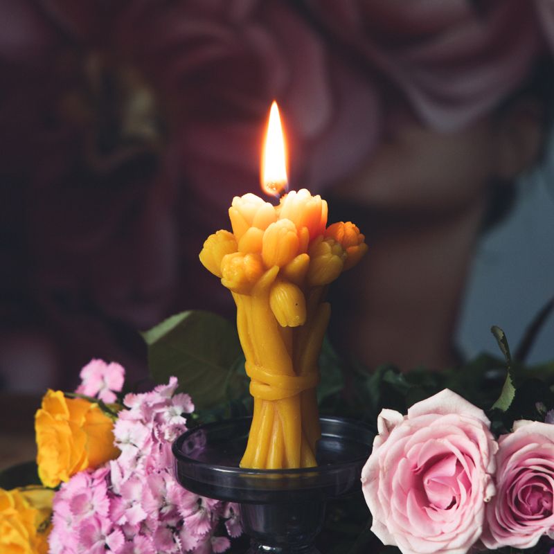 Brennende gelbe Wachskerze in Tulpenform. Auf einem Kerzenständer, umgeben von Blumen.