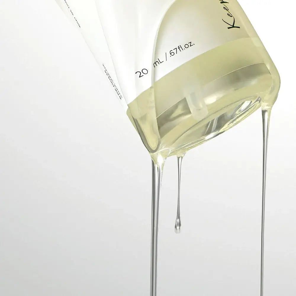 Klarflüssigkeit fließt aus einer transparenten Flasche. Aufschrift: 20 ml / 67 fl.oz. Einige Tropfen fallen herunter.
