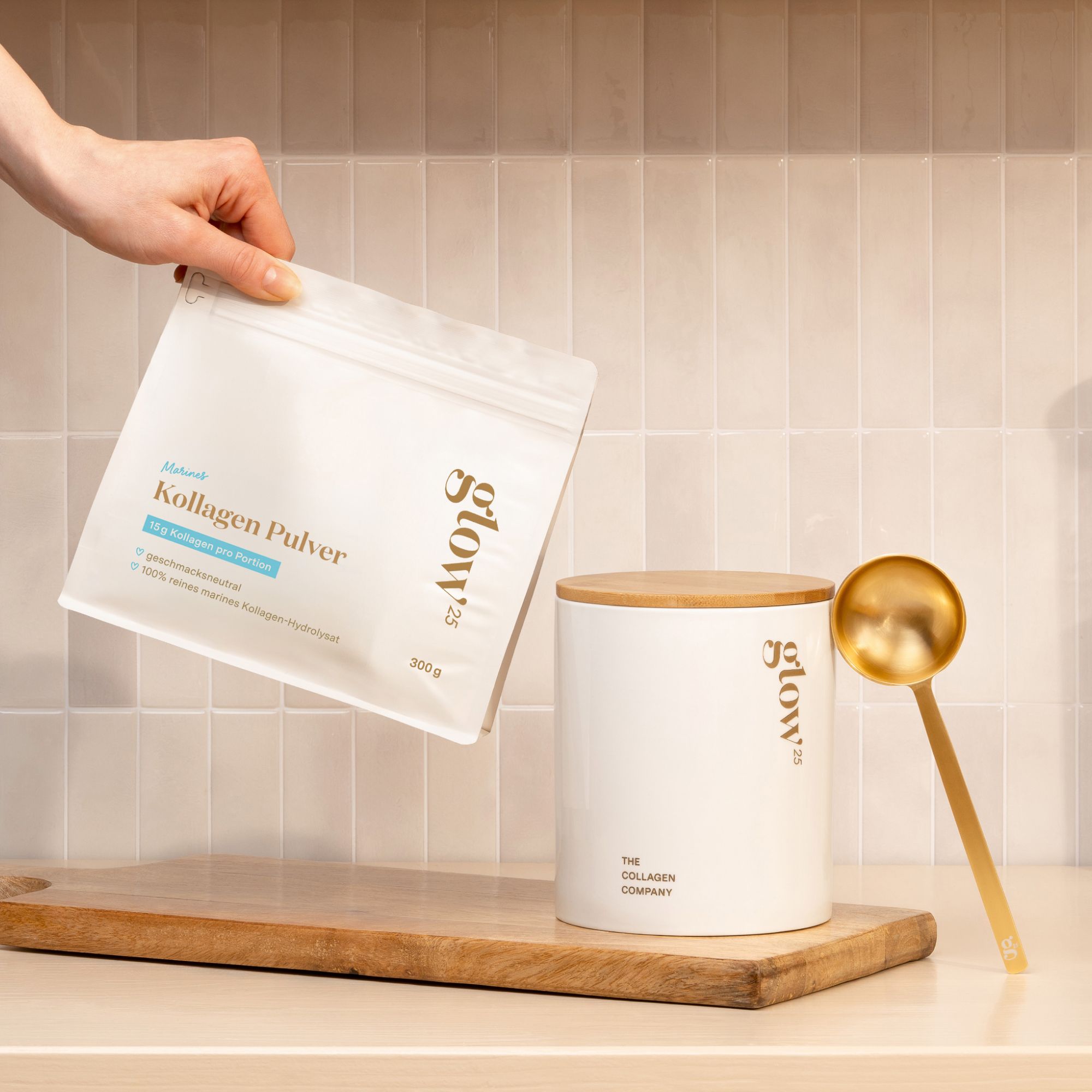 Hand hält eine weiße Tüte mit Kollagenpulver. Daneben ein weißer Behälter mit Holzdeckel und goldener Löffel. Aufschrift: Glow25.