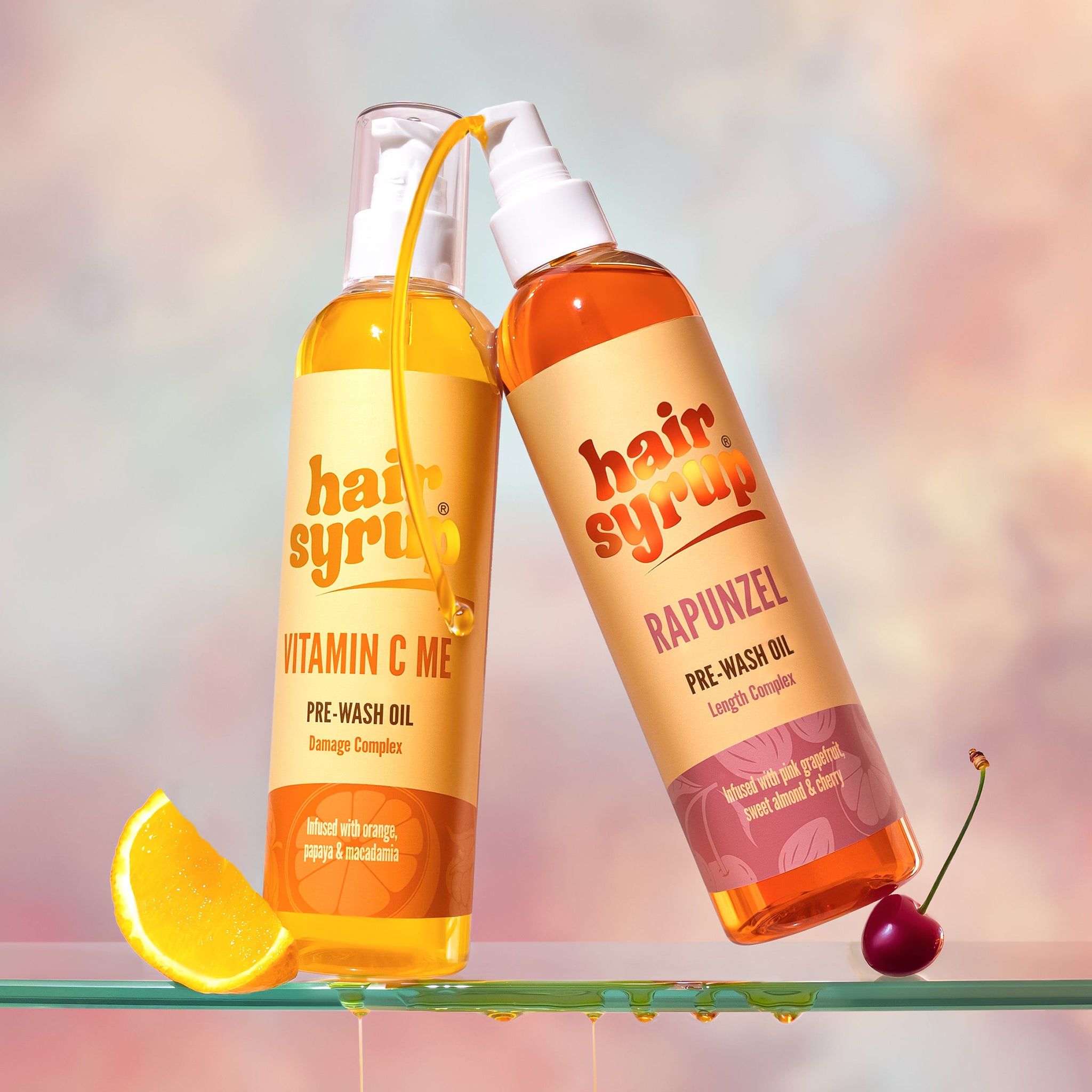 Zwei Flaschen "Hair Syrup"-Produkte. "Vitamin C Me" und "Rapunzel". Pre-Wash Oil. Auf Glasplatte.