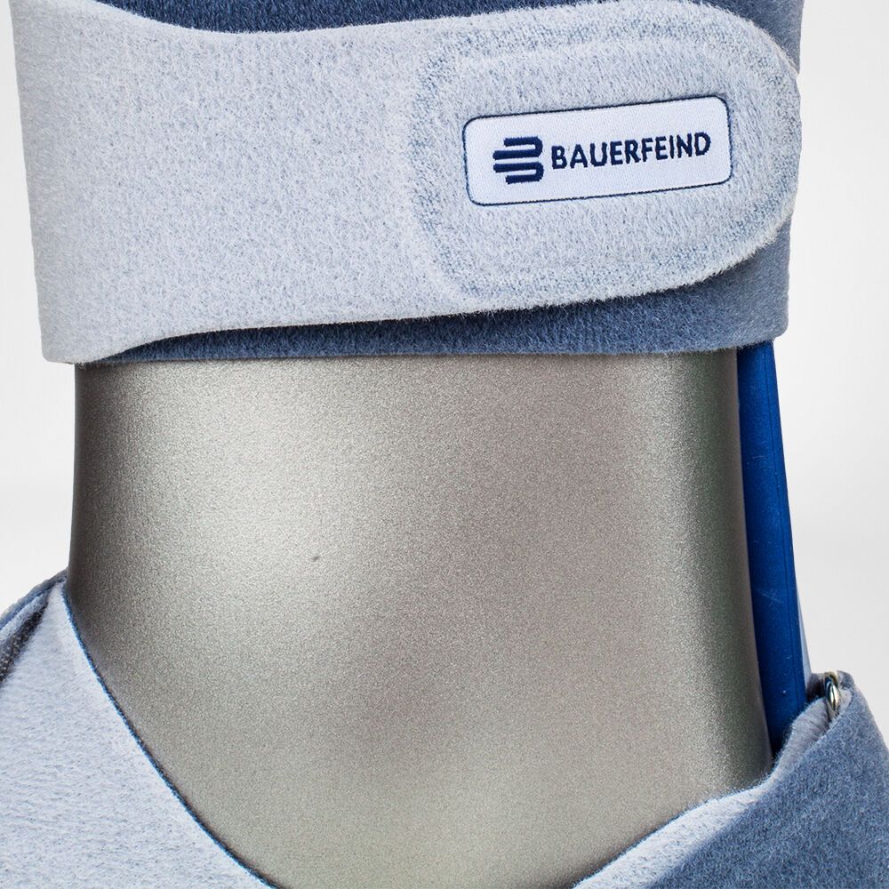 Knöchelorthese mit blauem Innenfutter. Klettverschluss mit Bauerfeind-Logo. Auf einem grauen Dummy.