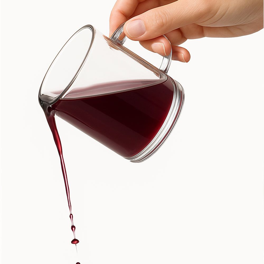 Glasbecher, der eine rote Flüssigkeit ausgießt. Flüssigkeit tropft nach unten.