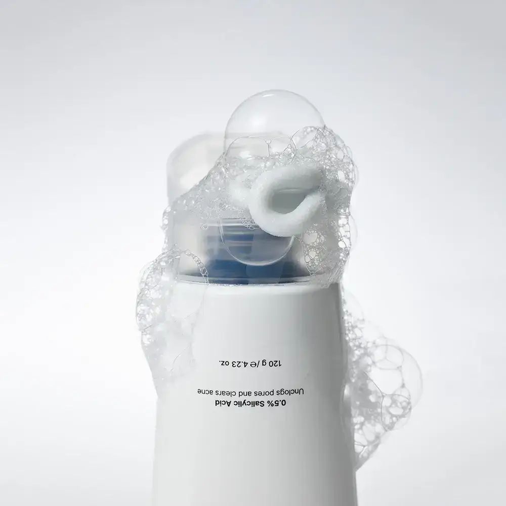 Weiße Tube mit Schaum. Aufschrift: 0.5% Salicylic Acid. 120 g / 4.23 oz. Schaum bedeckt die Oberseite.