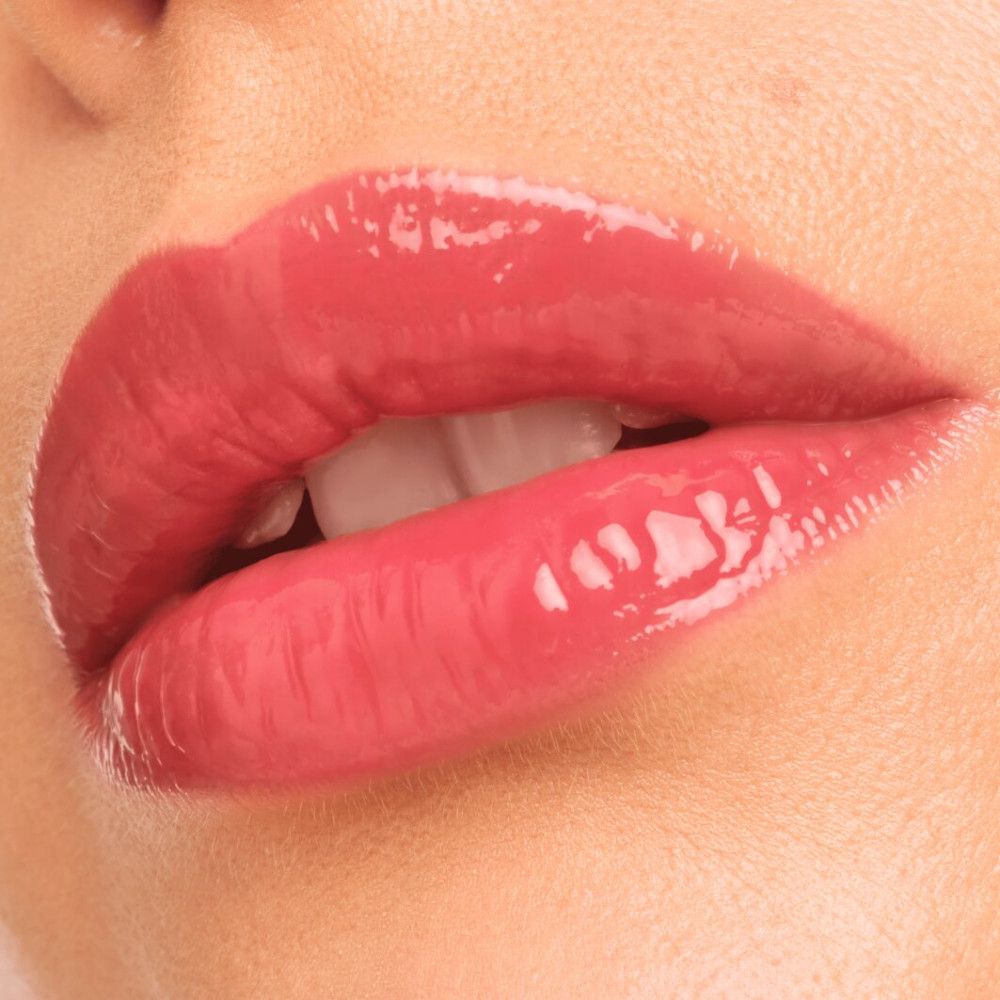 Nahaufnahme von Lippen mit glänzendem, rosa Lipgloss. Die Lippen sind leicht geöffnet, Zähne sichtbar.
