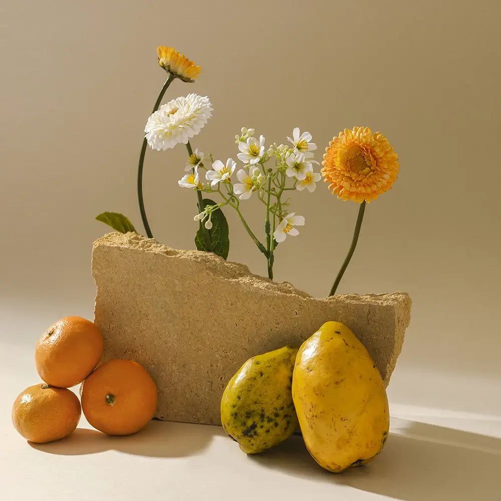 Arrangement mit Blumen, Mandarinen und Papayas. Blumen in einem Steinblock.