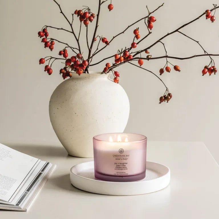 Rosafarbene Kerze mit drei Dochten auf einem weißen Tablett. Im Hintergrund eine Vase mit Zweigen und roten Beeren. Aufschrift: Chesapeake Bay.