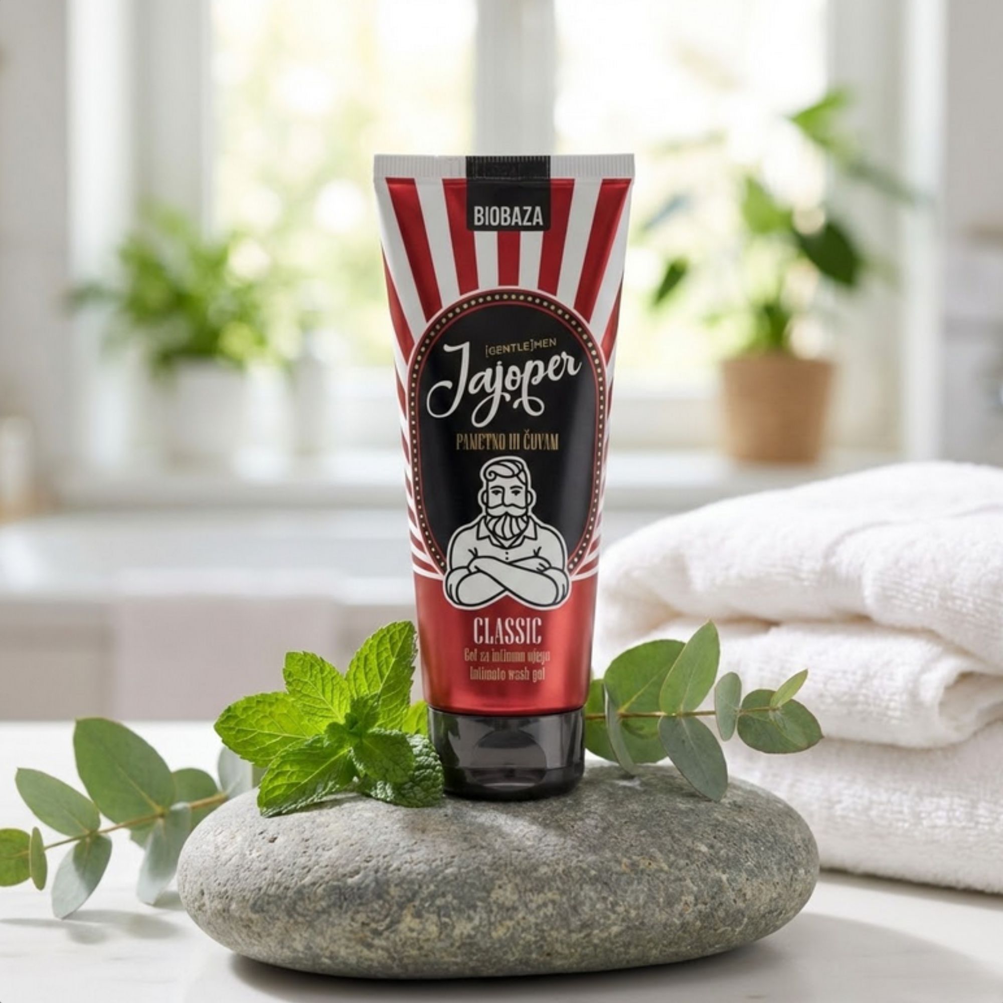 Tube mit rot-weißem Design. Aufschrift: Biobaza Jajoper Classic. Auf Stein, neben Minze und Handtüchern.