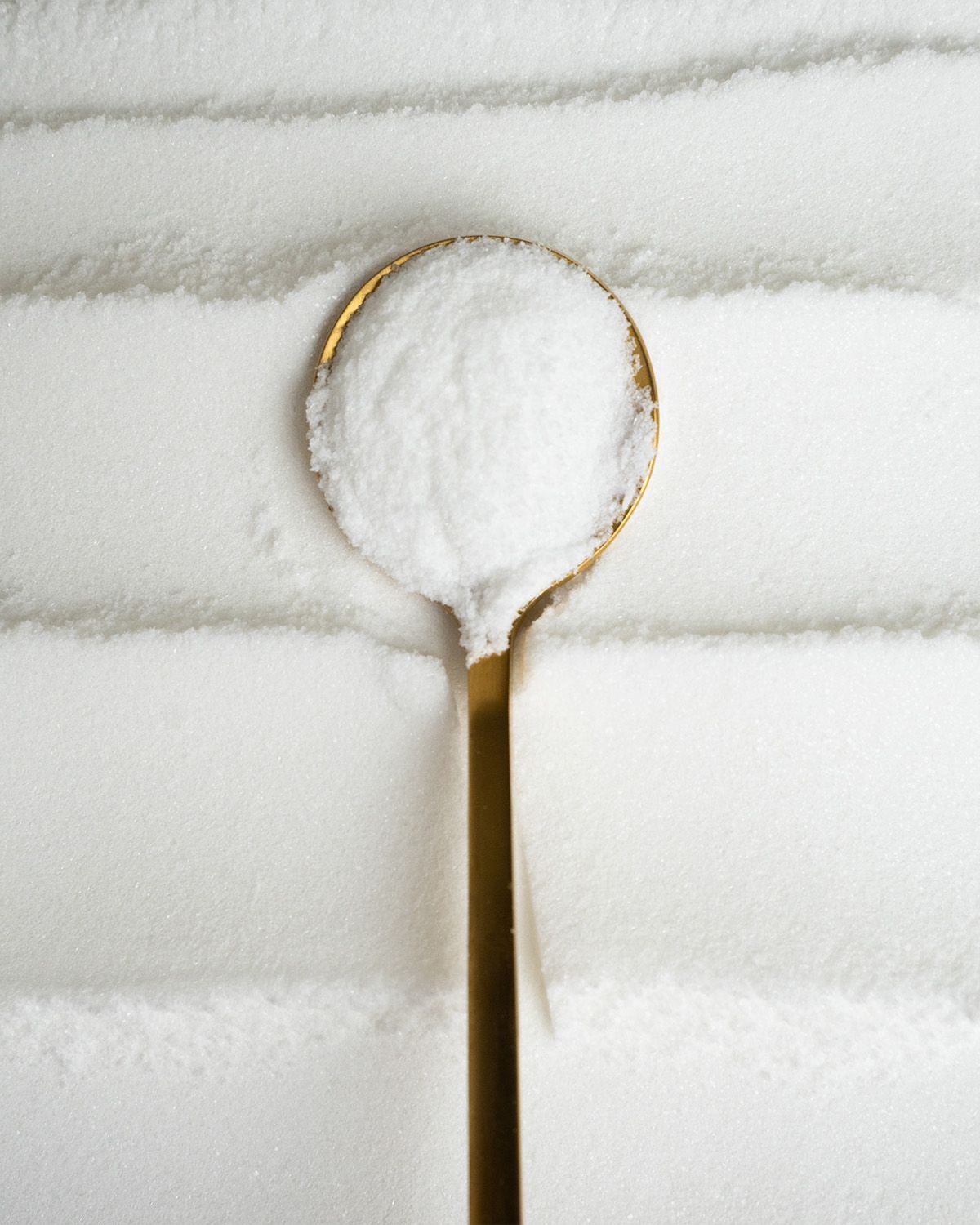 Ein goldener Löffel mit weißem Vitamin C Pulver auf gestreiften Pulverhintergrund.