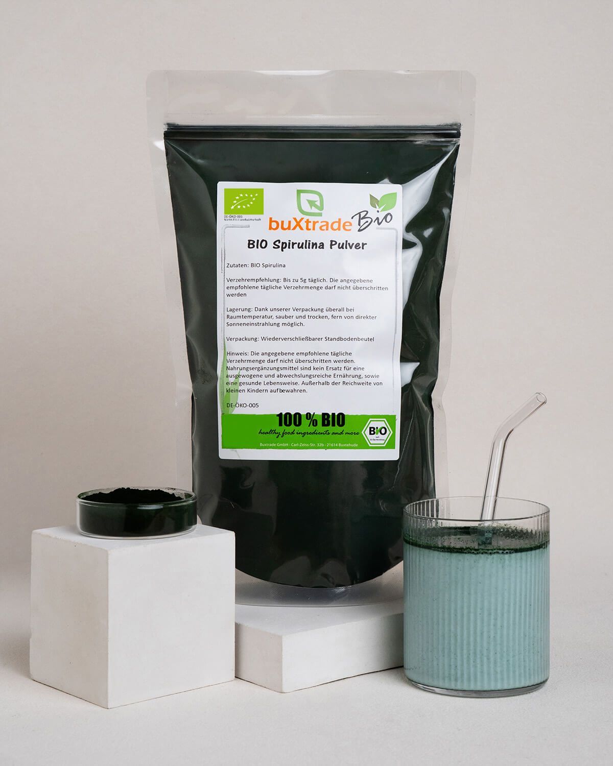 Verpackung mit Pulver, Glas mit Getränk und Schale mit Pulver auf Podesten.